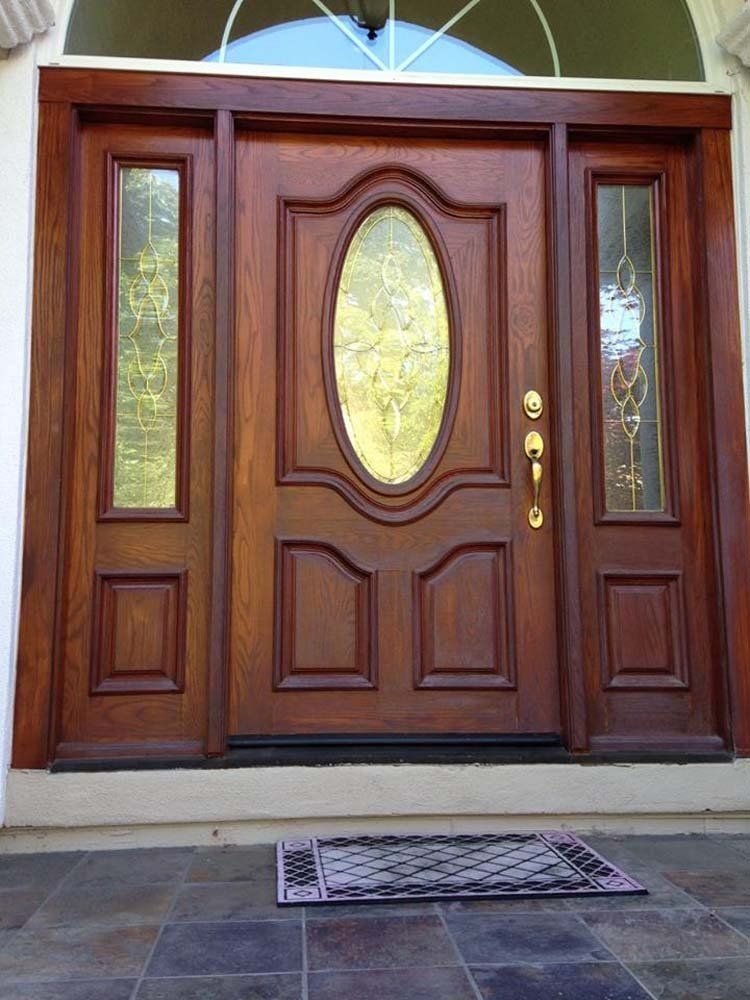 A large wooden door with a stained glass window and a rug in front of it.