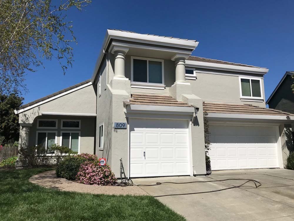 A large white house with two garage doors and a blue sky in the background.