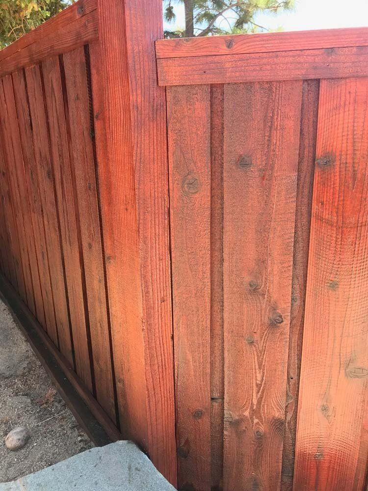 A close up of a red wooden fence next to a sidewalk.