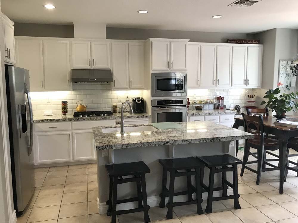 A kitchen with white cabinets , granite counter tops , stainless steel appliances and a large island.