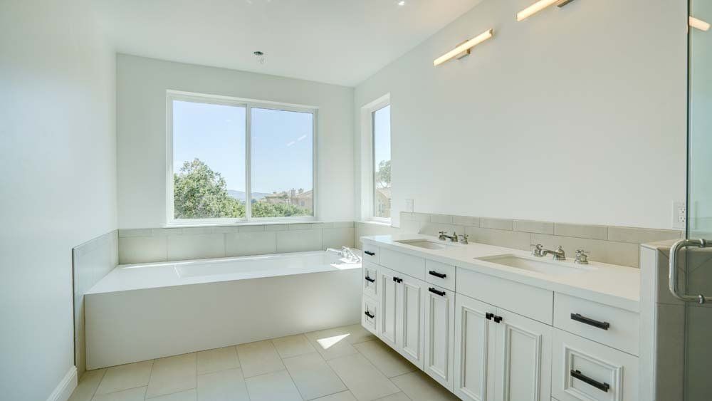 A bathroom with two sinks , a tub and a window.