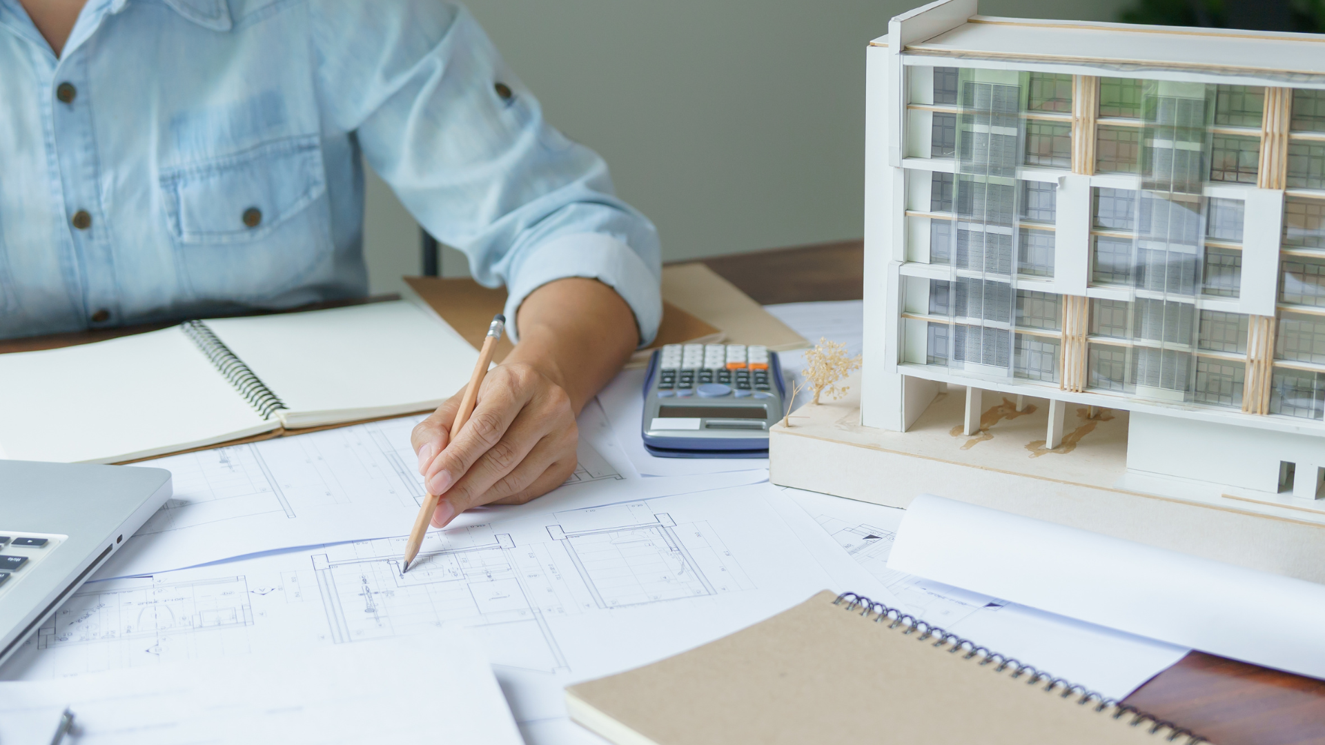 Construction worker holding blueprints at a construction site, wearing a reflective vest.