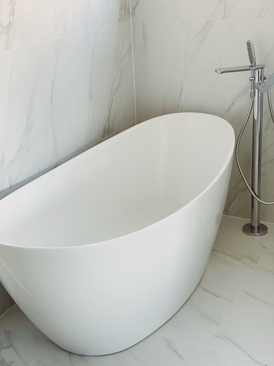 A White Bathtub is Sitting in a Bathroom Next to a Marble wall — Illawarra Bathrooms in Wollongong, NSW