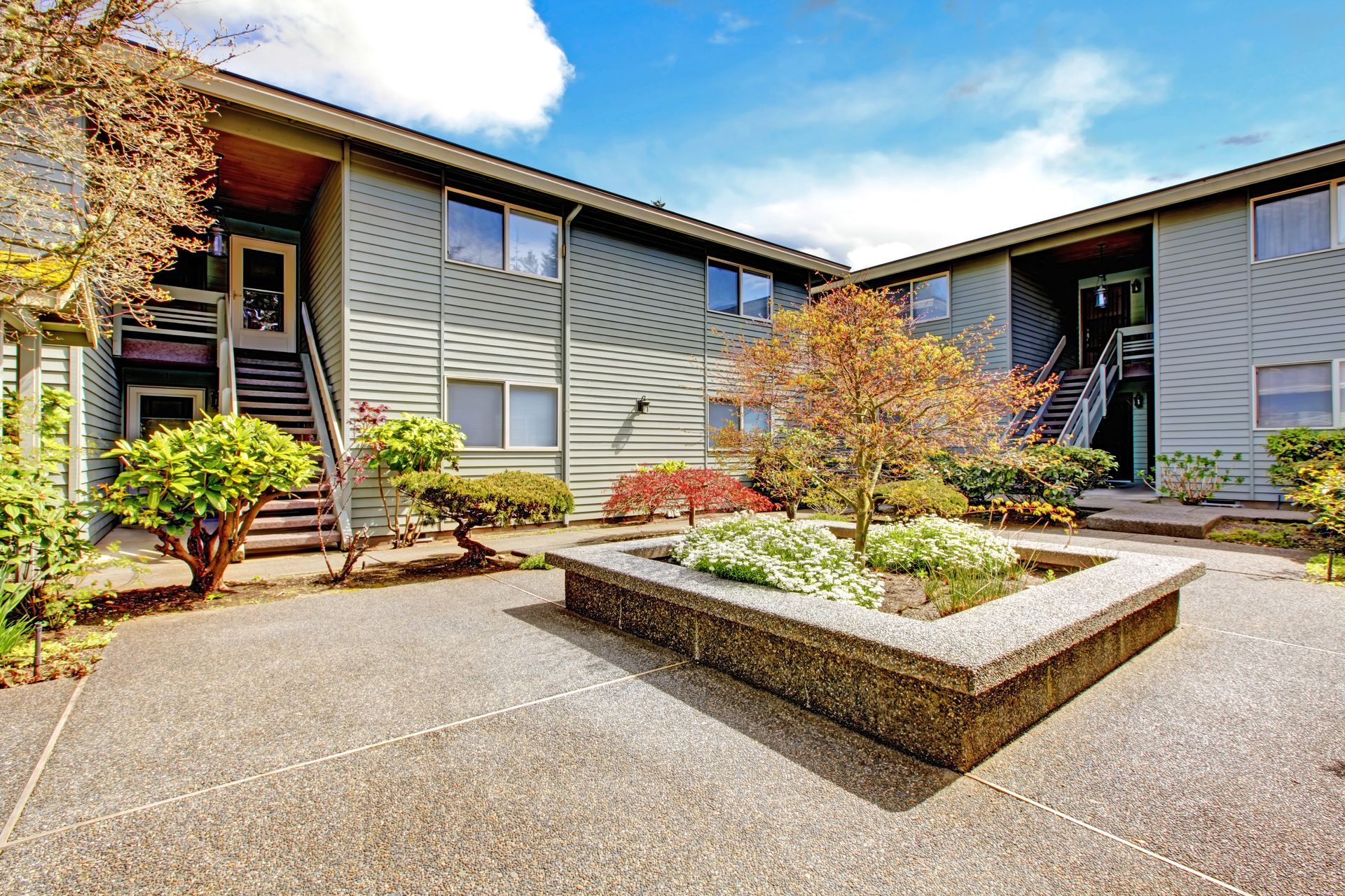 Courtyard of a two-story apartment complex with green siding, a central planter, and stairs to units.