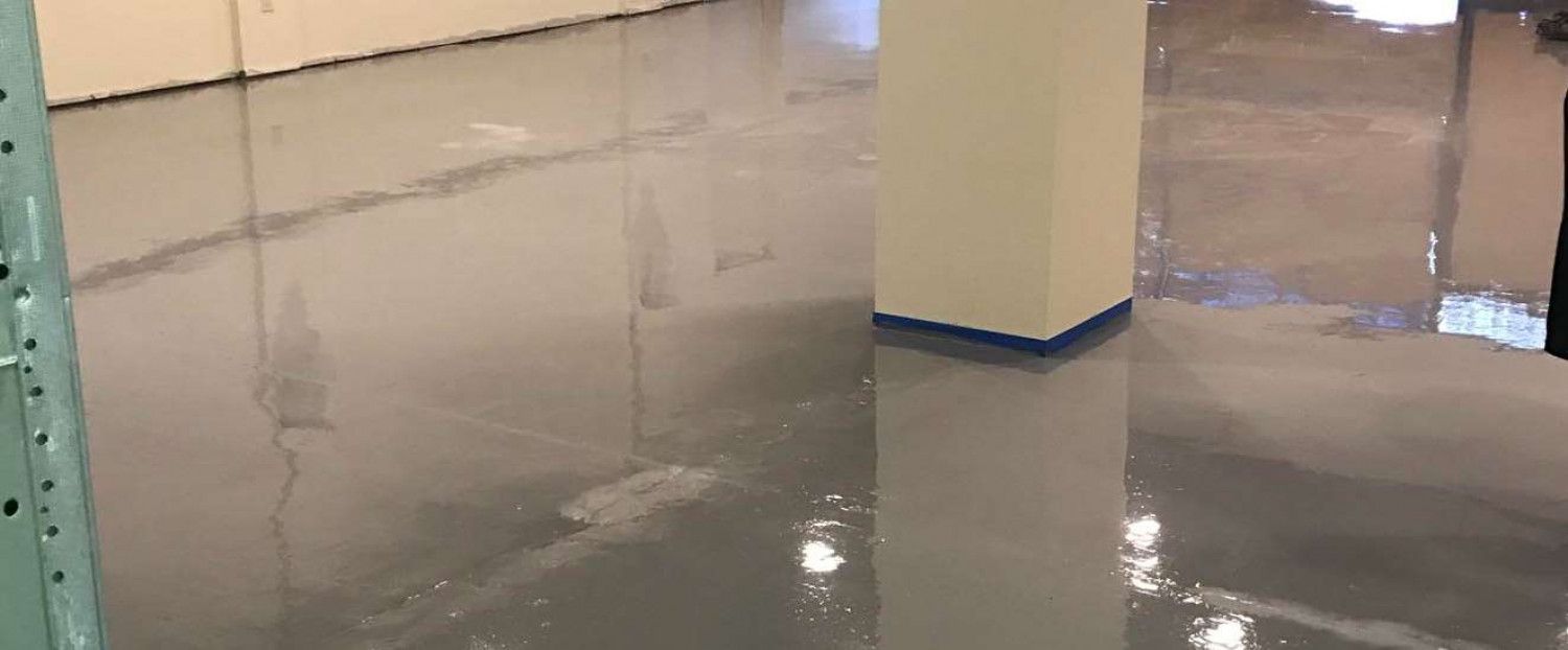 A room with a shiny, gray epoxy floor and white walls. There is a white pillar on the right side of the frame.