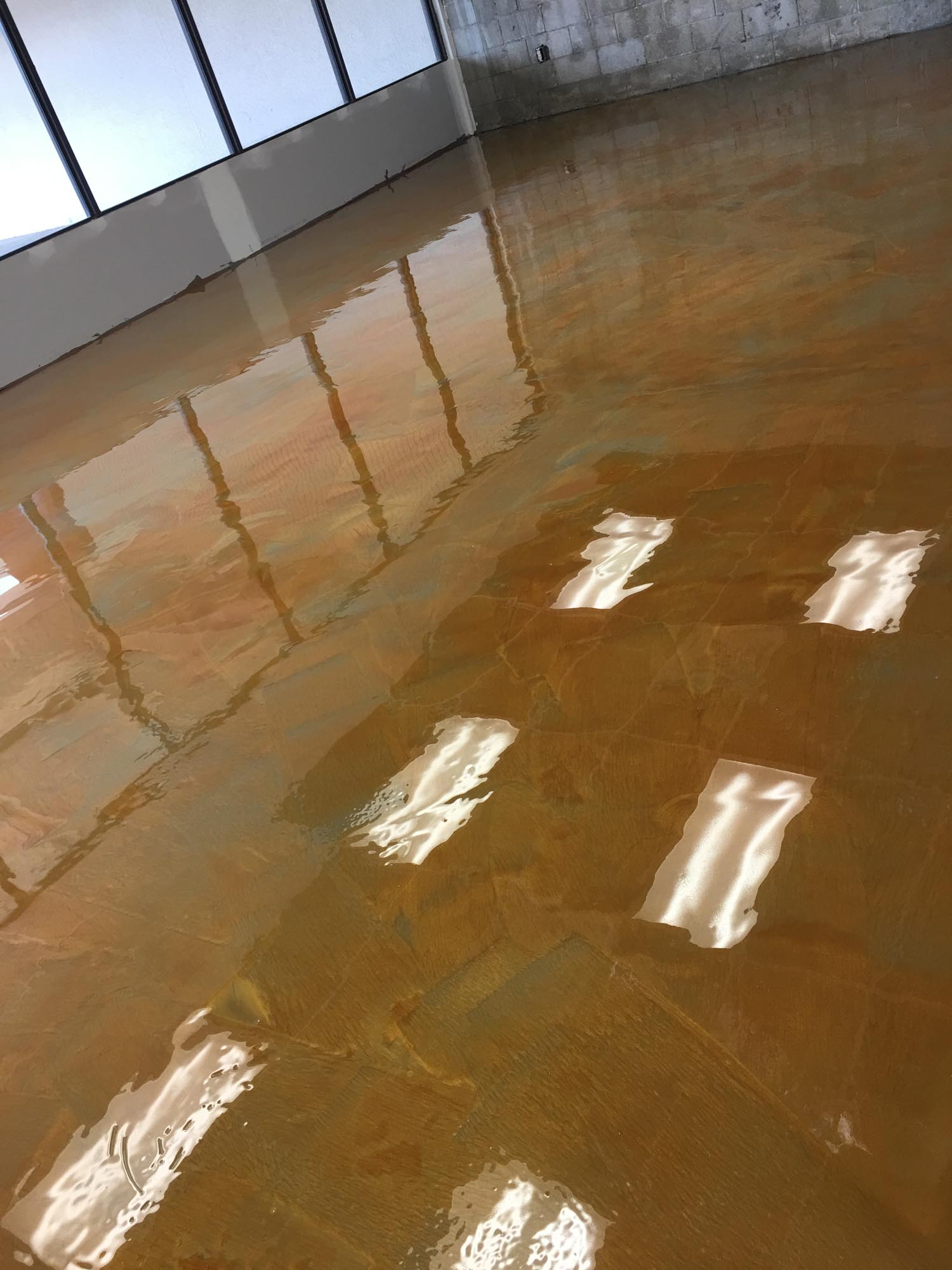 Golden-brown, glossy epoxy floor reflecting light from windows and ceiling fixtures in an interior space.