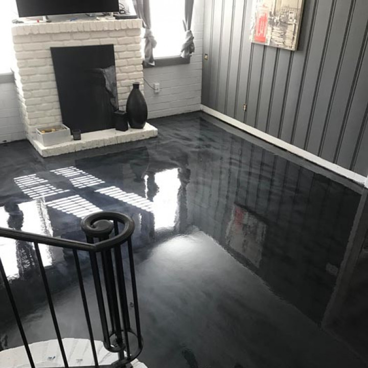 Dark gray epoxy floor reflects the room's features: fireplace, stairs, and art.
