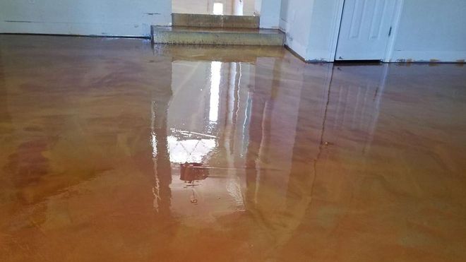 Metallic epoxy floor, orange and gold hues, reflecting light, interior setting with stairs and white walls.