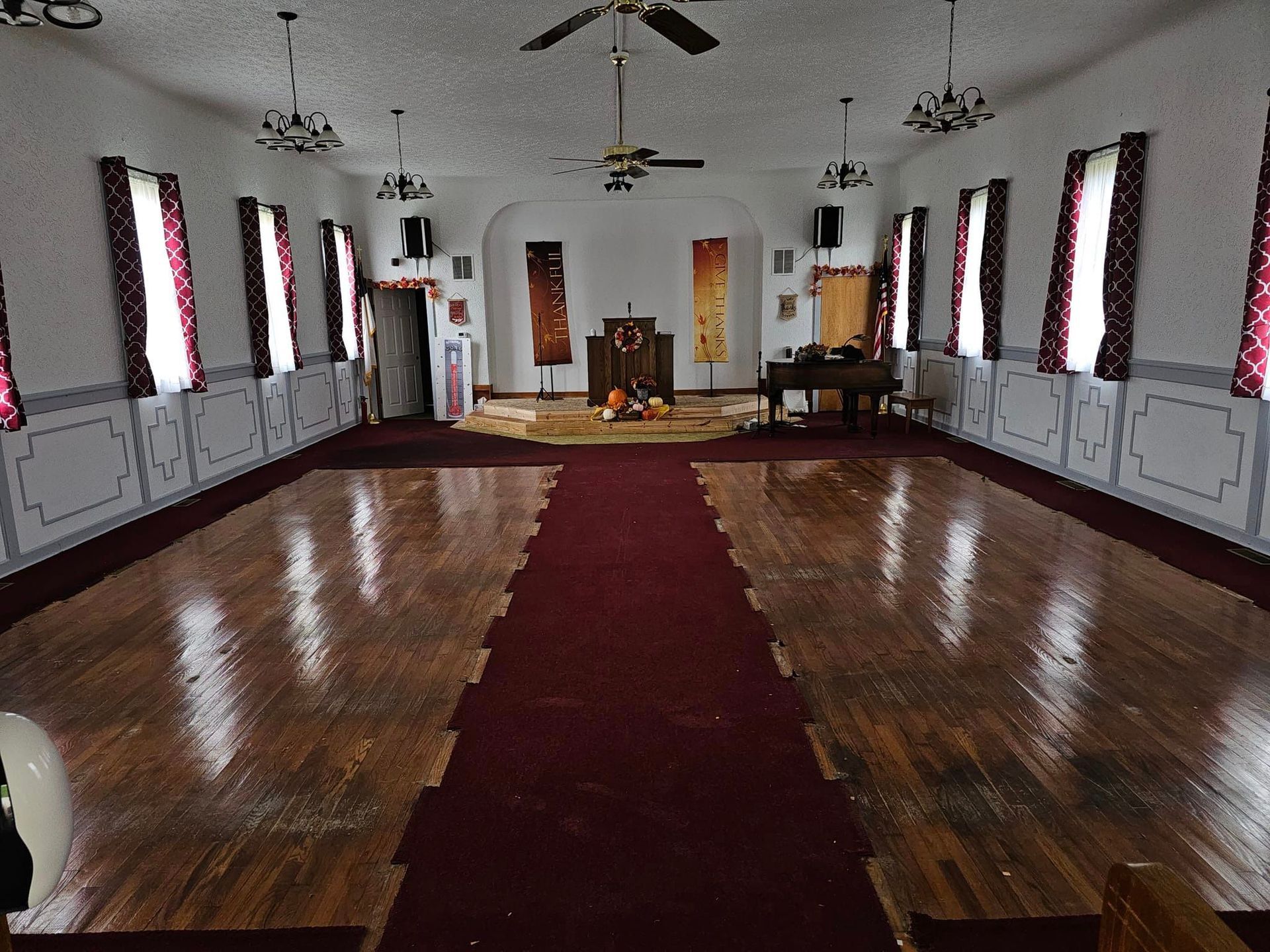 Interior of a hall with a red carpet runner, wood floor, white walls with windows and red curtains.