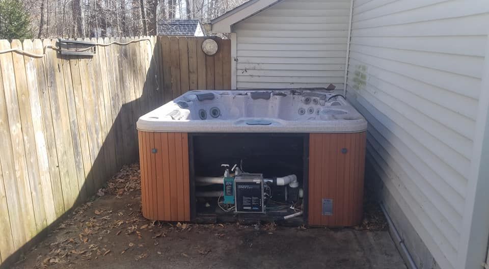 Hot tub nestled between a wooden fence and house, with open panel revealing internal mechanics.