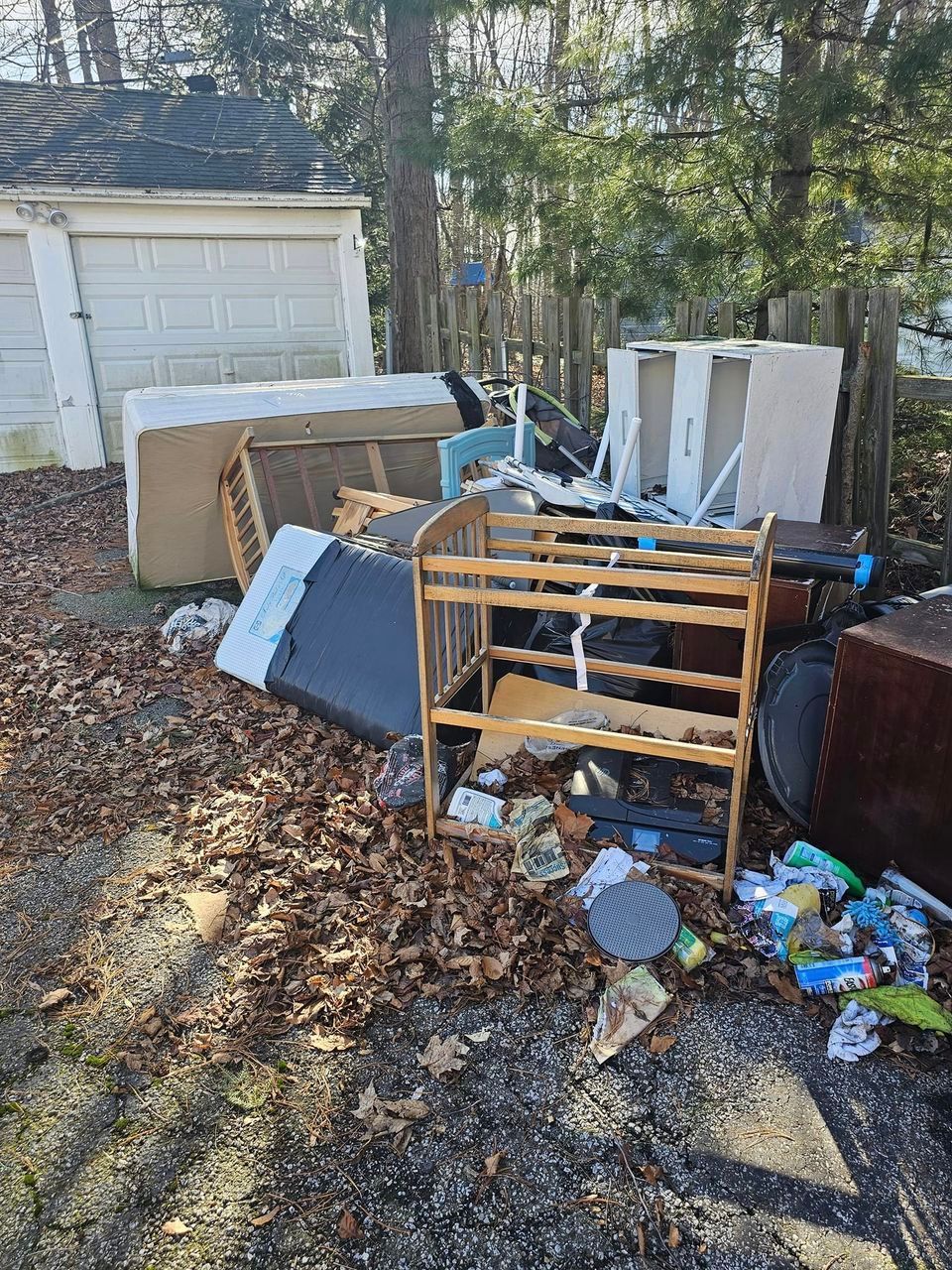 Pile of discarded furniture and trash in a backyard; includes a crib, cabinets, and a garage.
