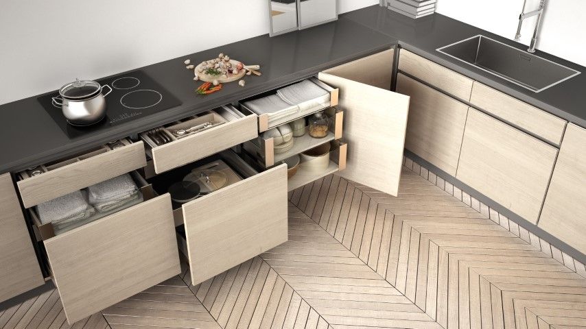 Modern kitchen with open drawers. Light wood cabinets, black countertop, stainless steel sink, and parquet floor.