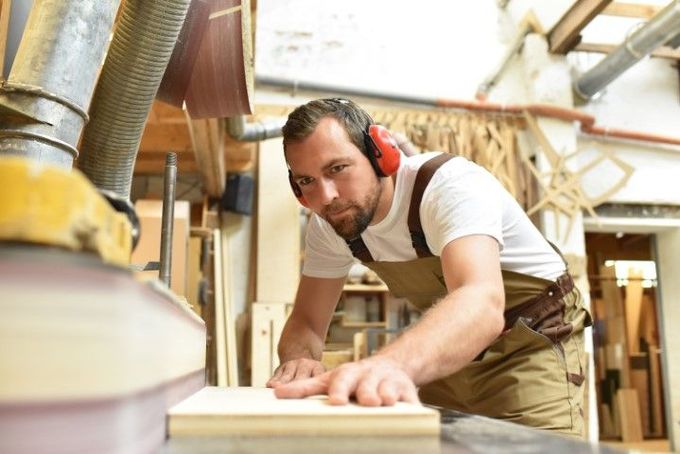 Carpenter sanding wood, wearing ear protection, in a workshop.
