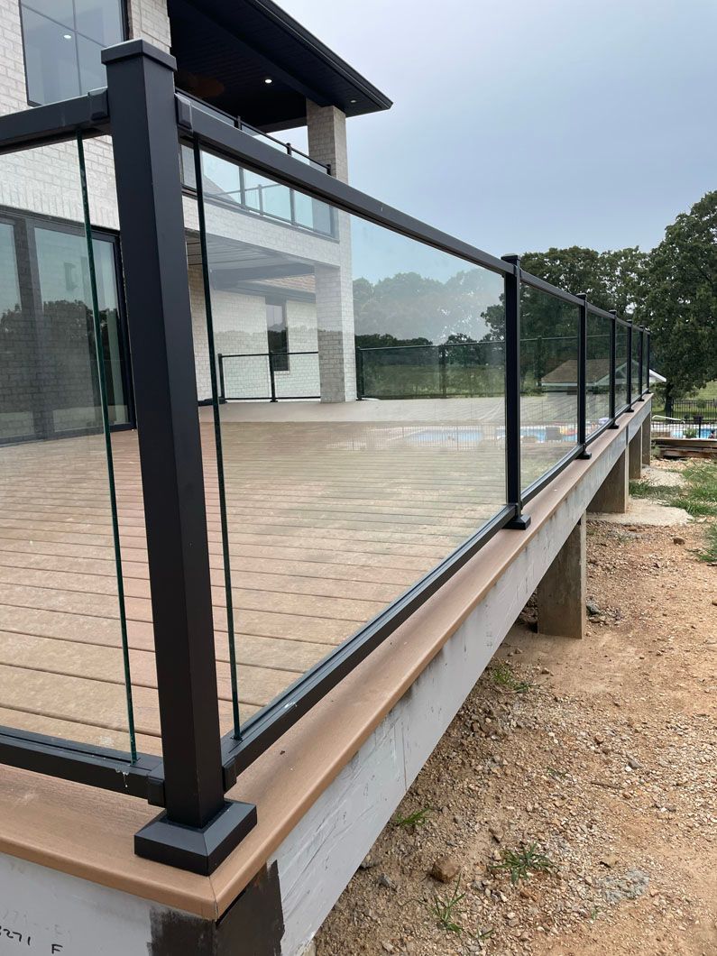A deck with a glass railing and a house in the background.