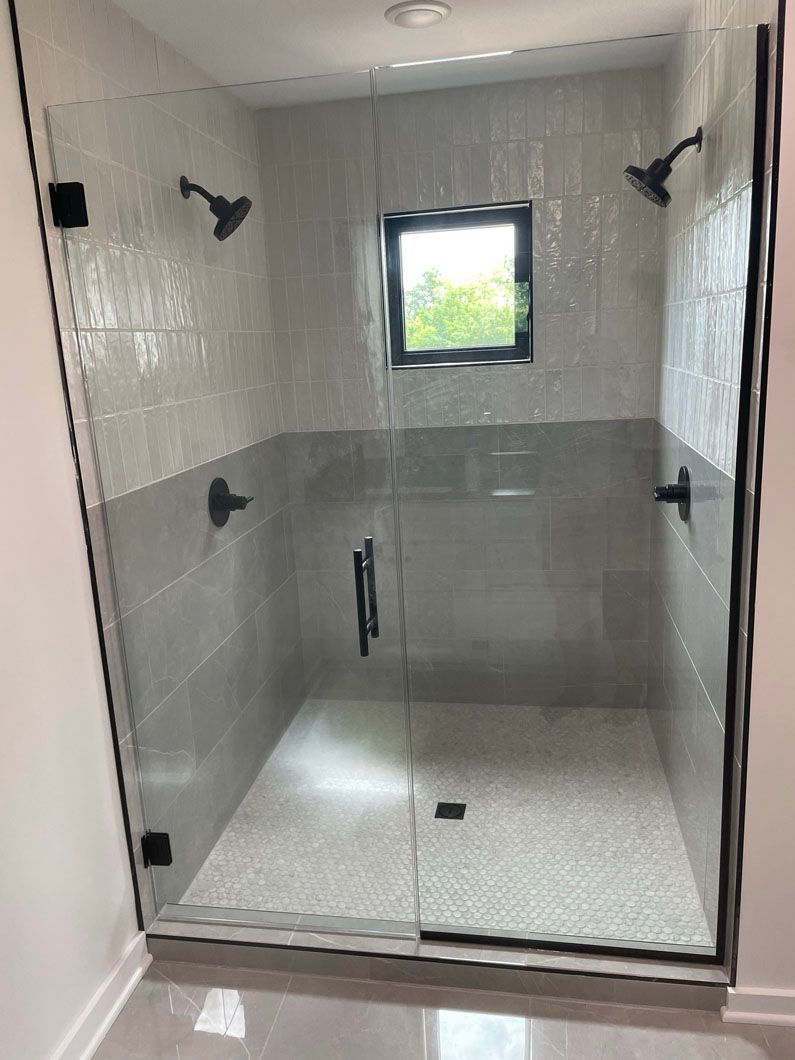 A bathroom with a walk in shower with a glass door and a window.