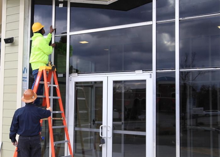 A man on a ladder is working on a glass door