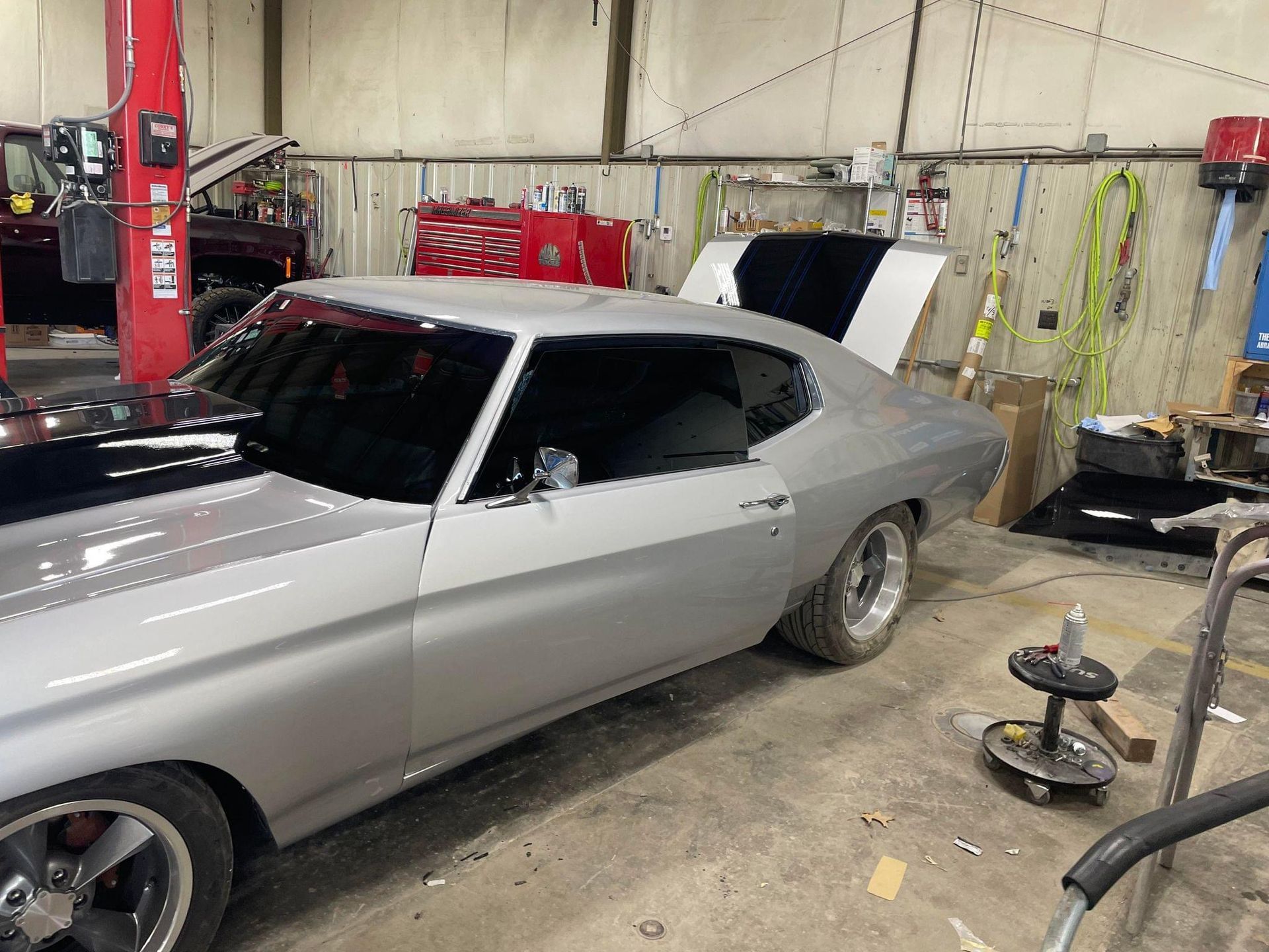 A silver car is parked in a garage with the hood open.