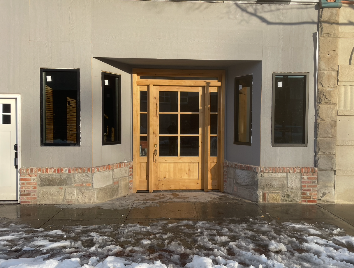 A gray building with a wooden door and windows