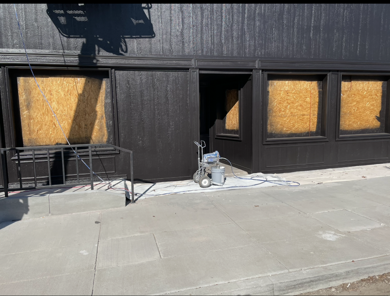 A black building with a spray painter on the sidewalk in front of it.