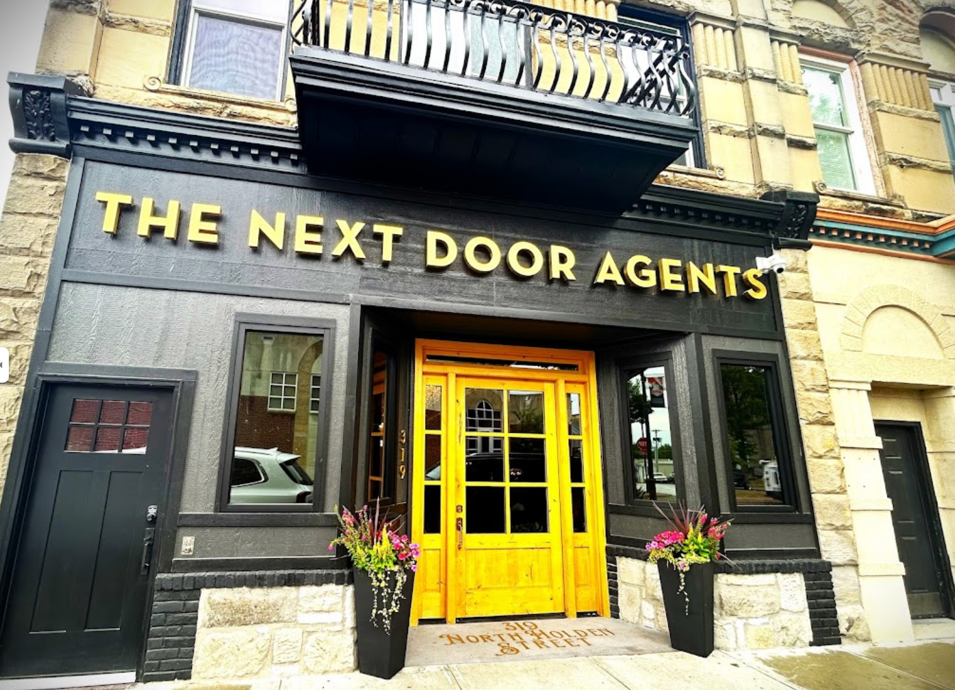 A building with a yellow door and a sign that says the next door agents