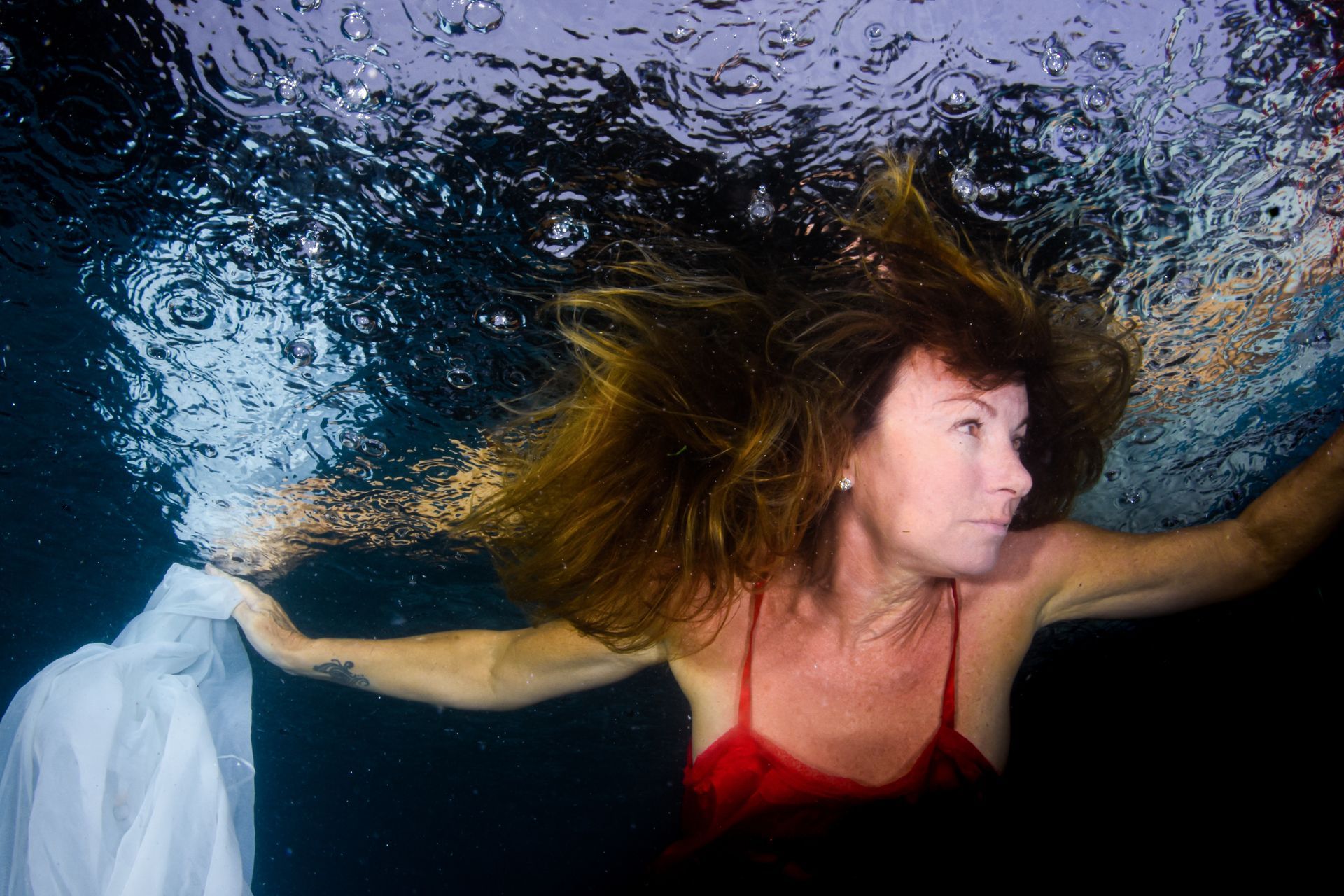 A fine art portrait of a Fiji bride swimming under rain drops holding red flowers