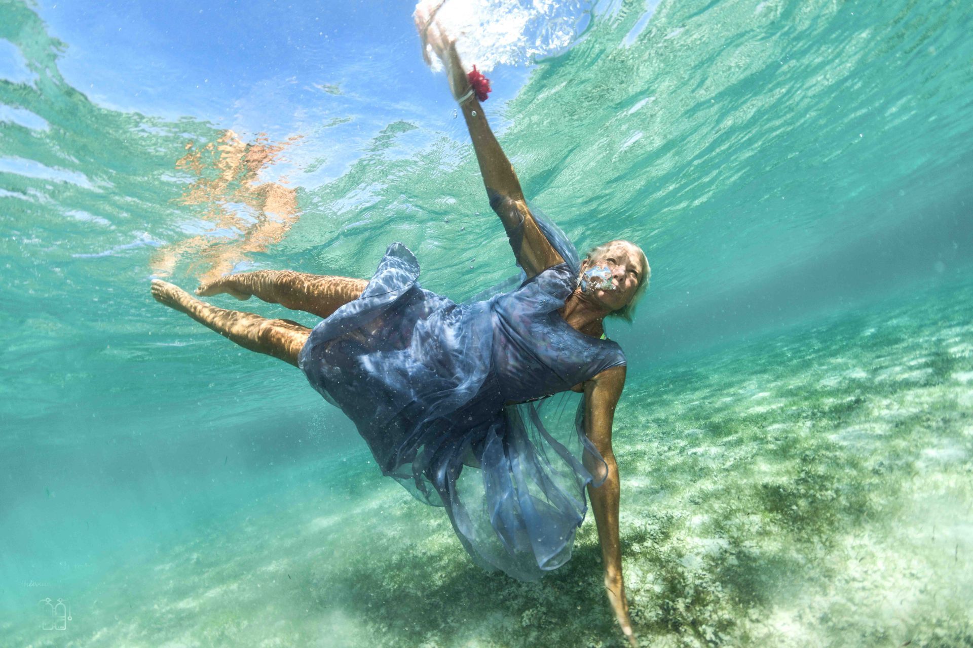 A blonde haired lady posing in Fiji's turquoise waters wearing a pale blue dress