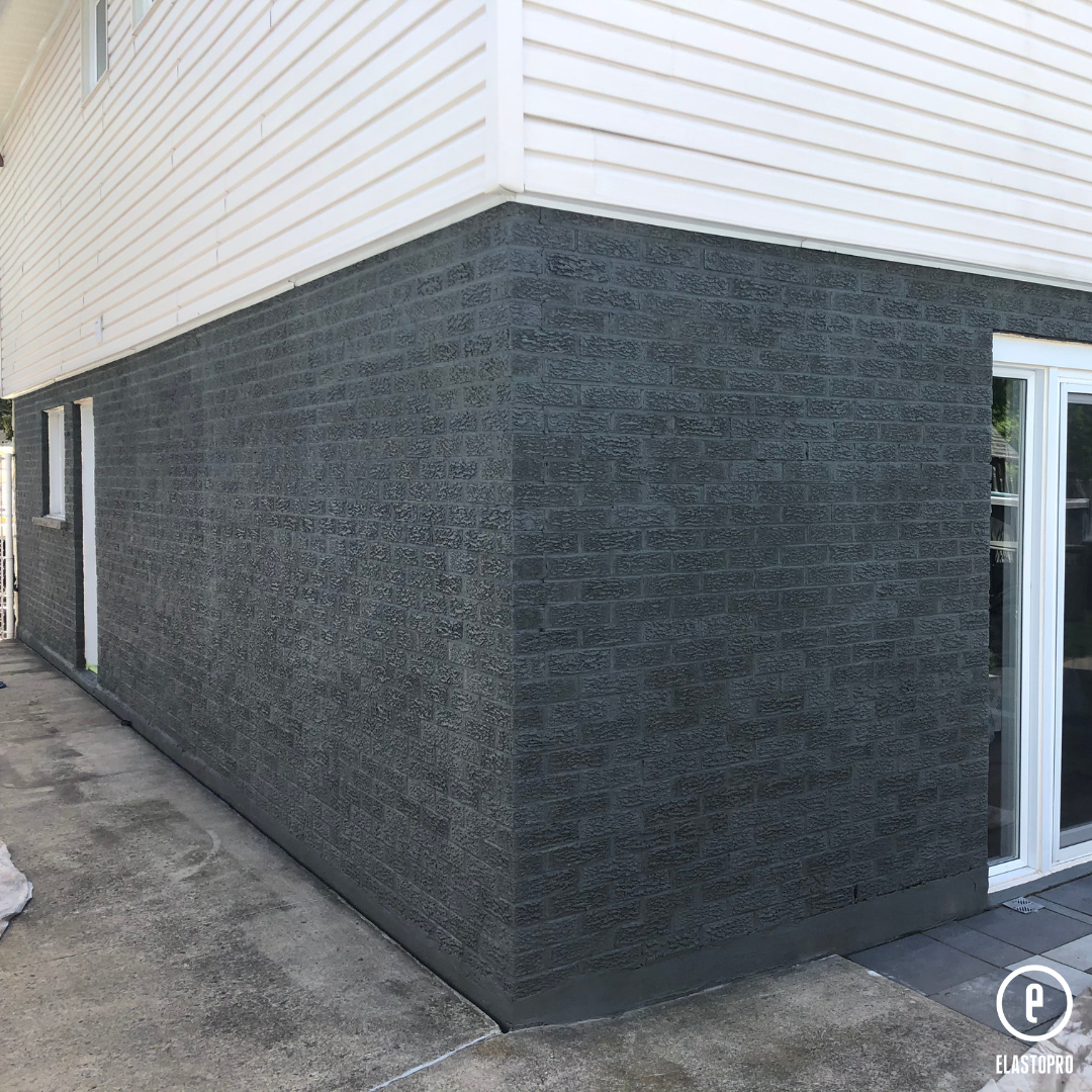 le côté d'une maison avec un mur de briques noires et un parement blanc.