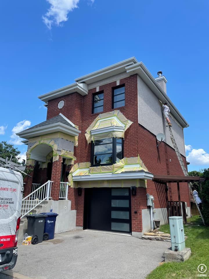 un homme peint le côté d'une maison en brique.