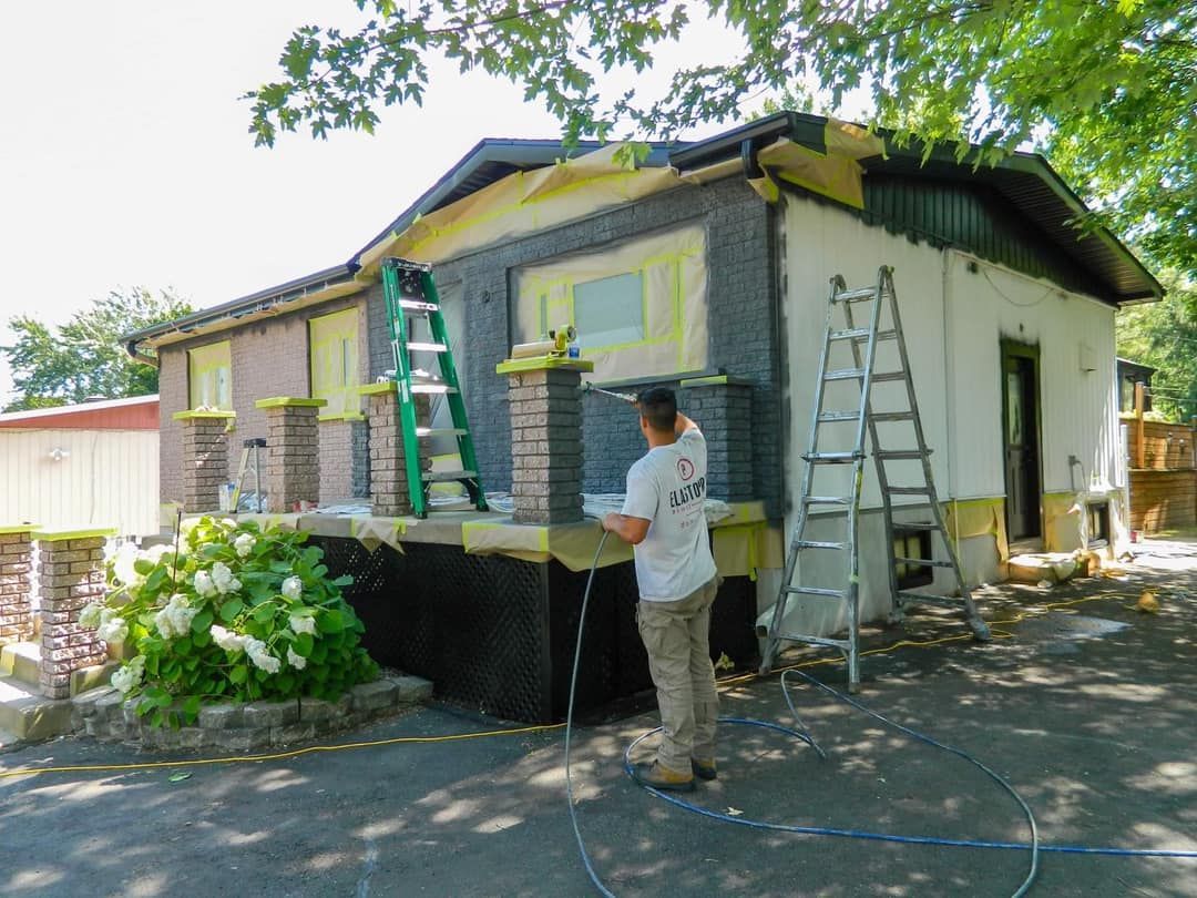 Une personne travaille à l'extérieur d'une maison, des échelles sont présentes, des travaux de construction sont en cours.