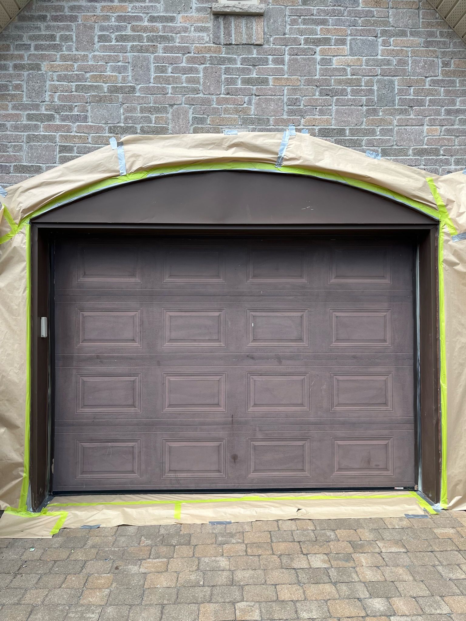 une porte de garage est en train d'être peinte devant un bâtiment en brique.