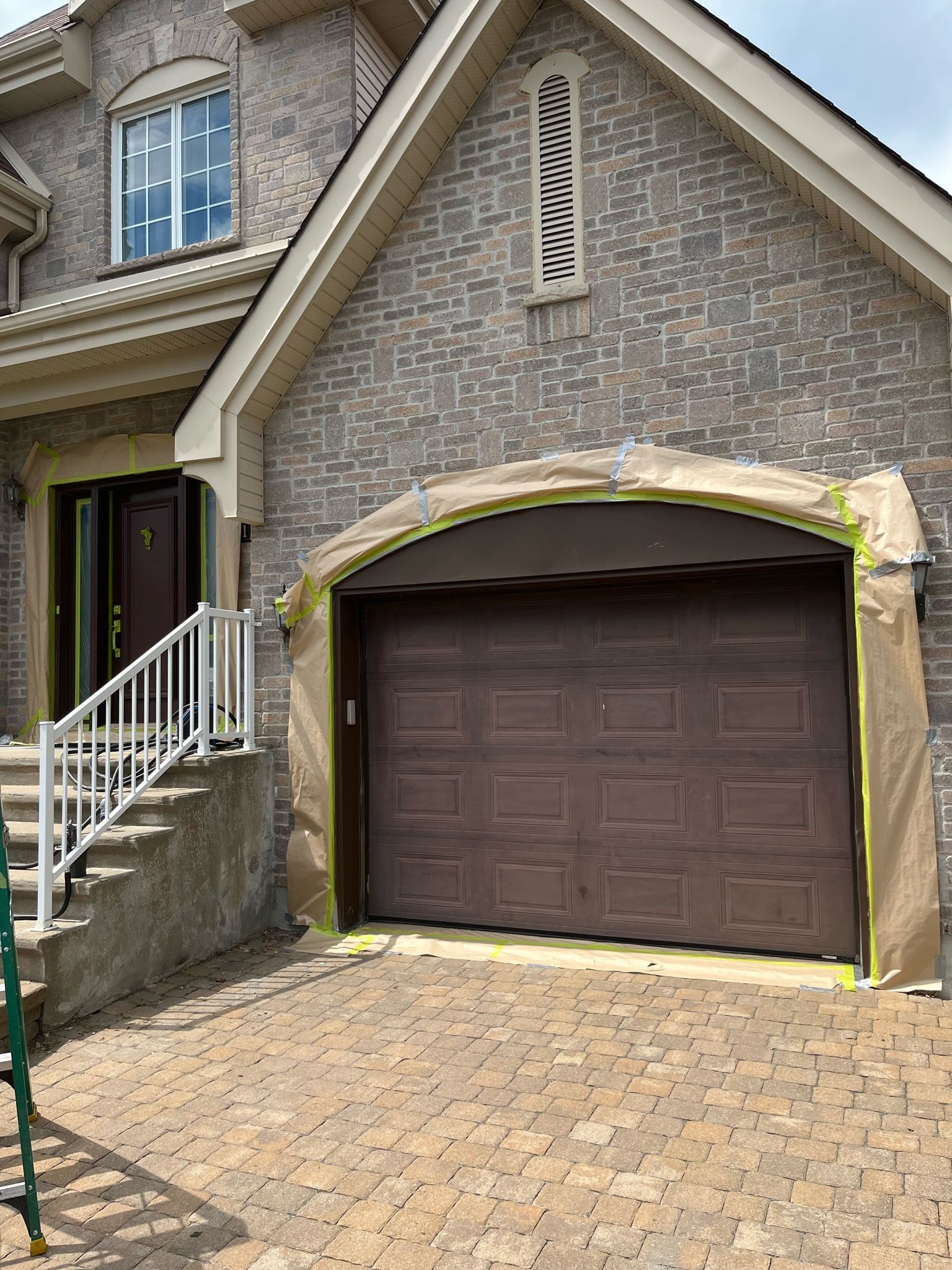 une grande maison en brique avec une porte de garage marron est en cours de peinture.