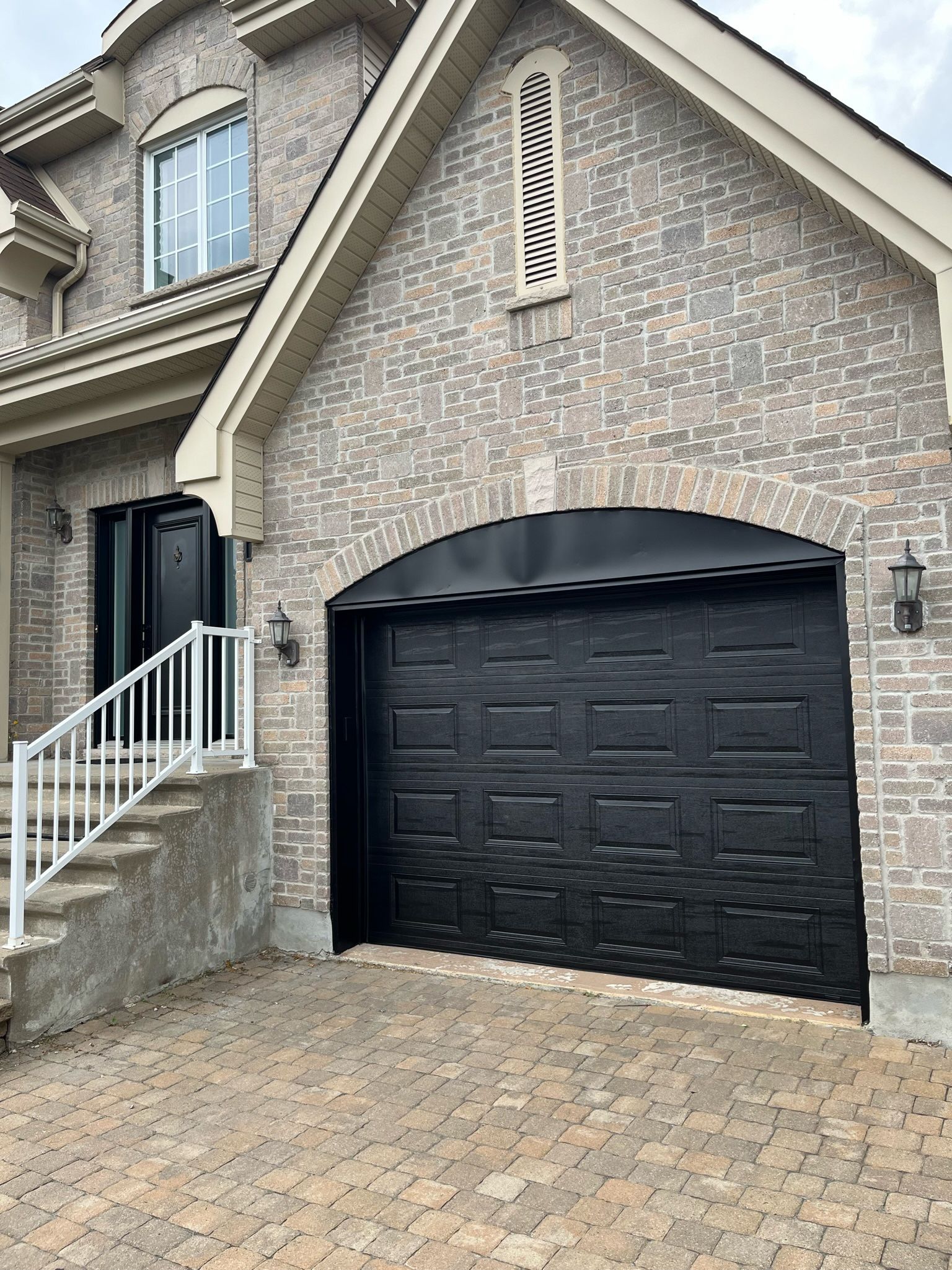 une grande maison en brique avec une porte de garage et des escaliers noirs.