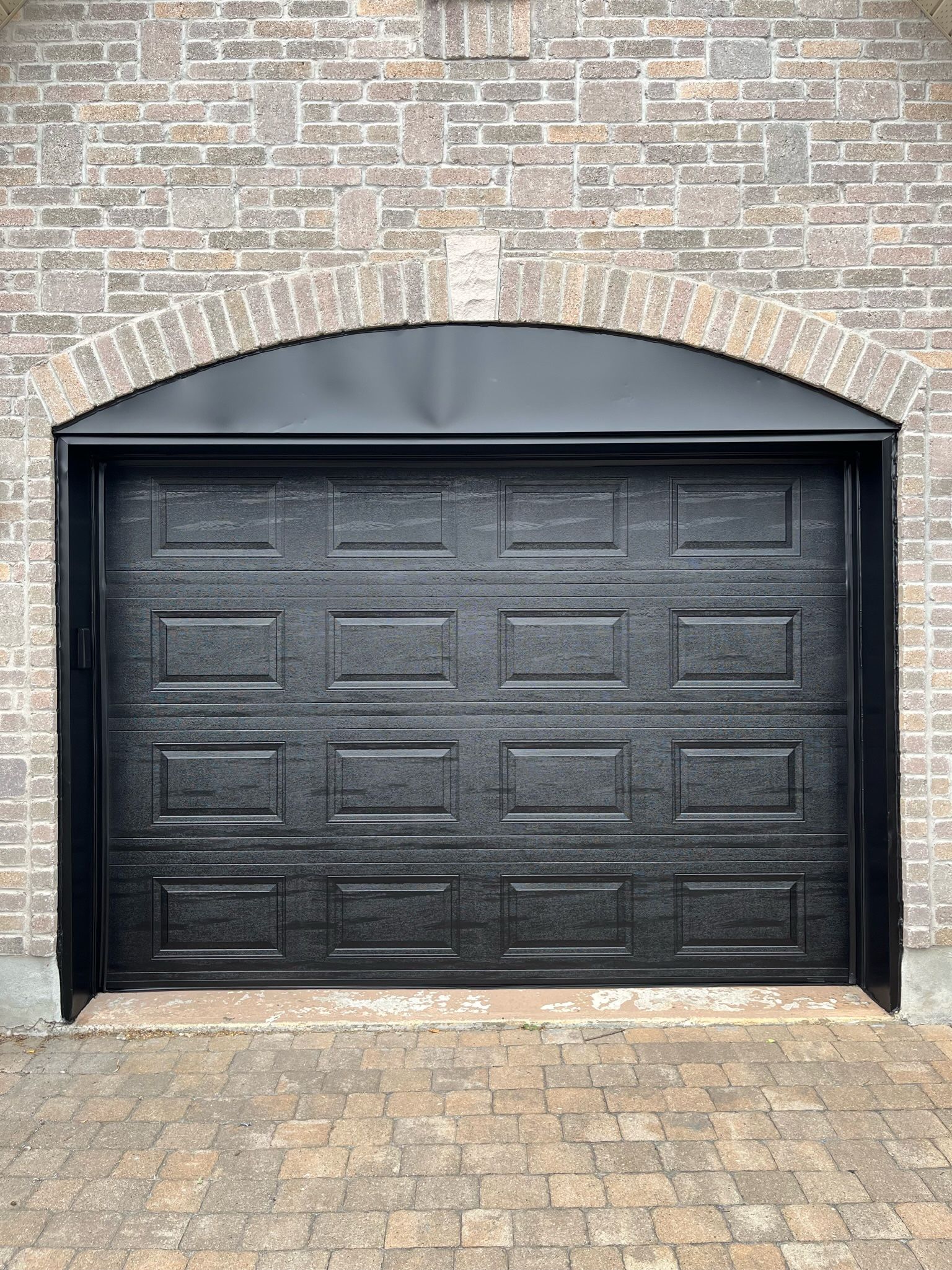 une porte de garage noire se trouve devant un mur de briques.