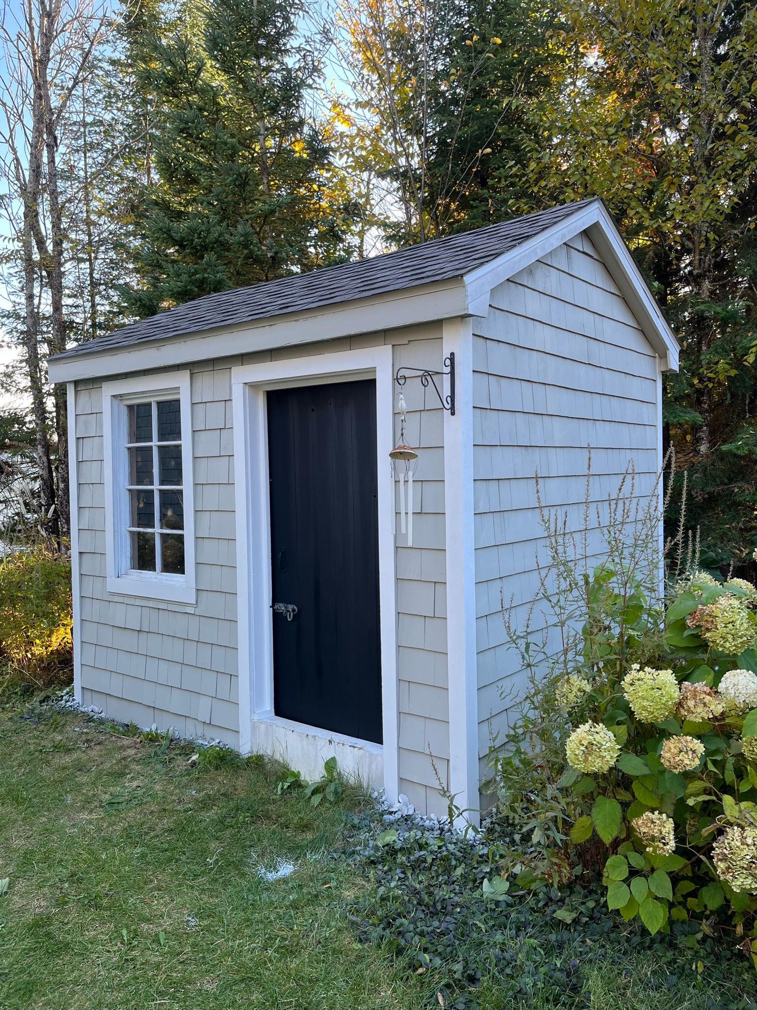 un petit hangar blanc avec une porte et une fenêtre noires est posé dans l'herbe.