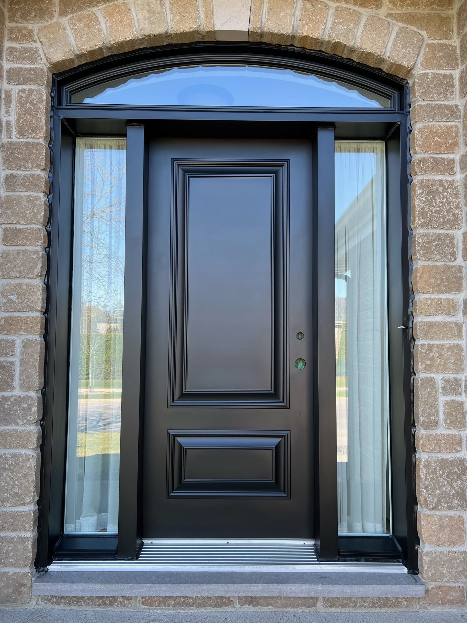 une porte d'entrée noire avec une fenêtre dans un bâtiment en brique.