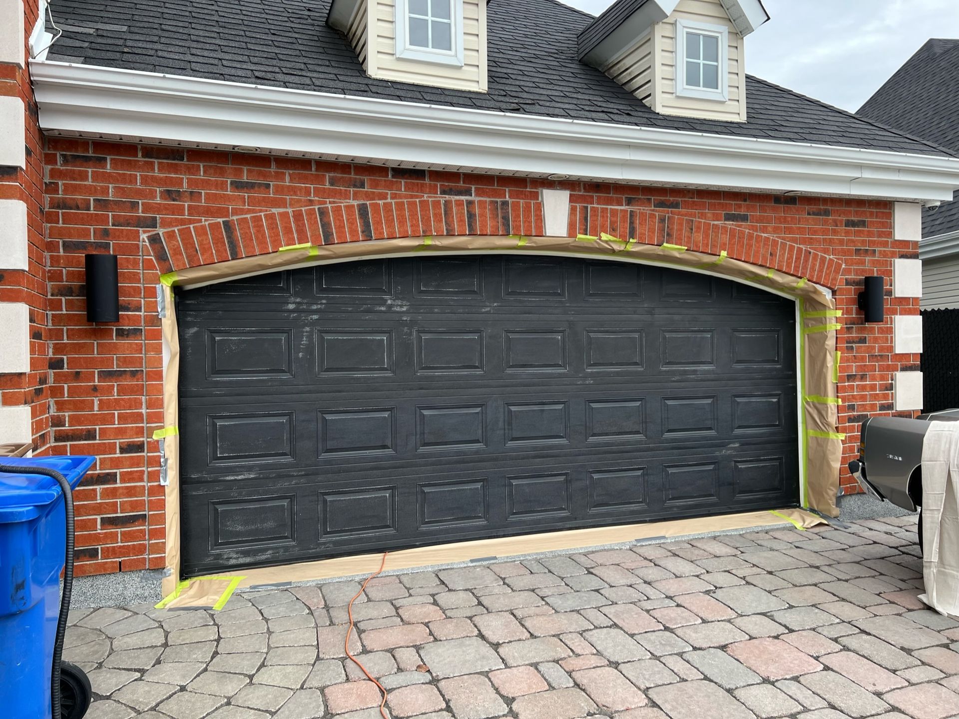 Une porte de garage noire est peinte sur une maison en briques rouges.