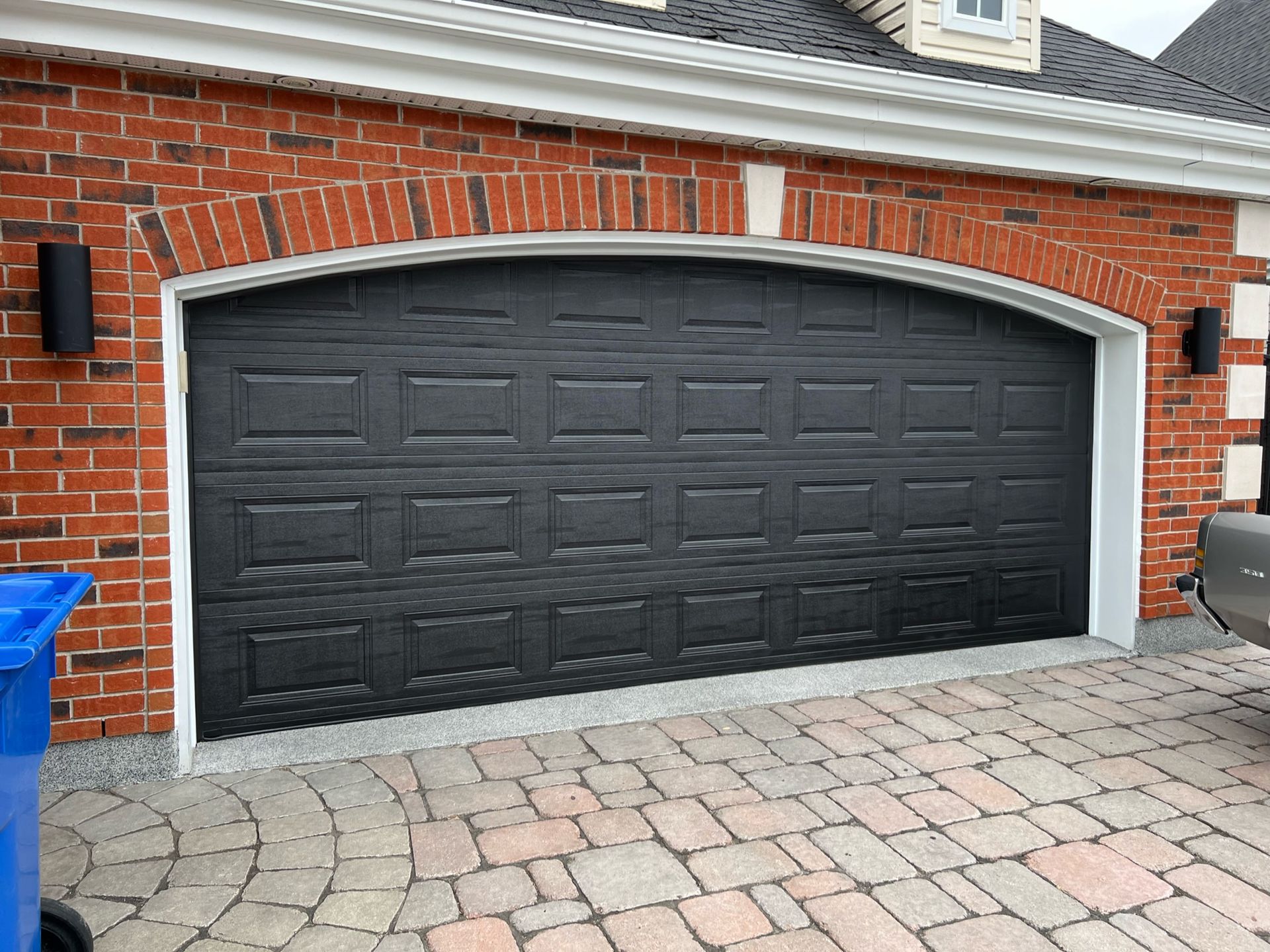 une porte de garage noire se trouve devant une maison en briques rouges.