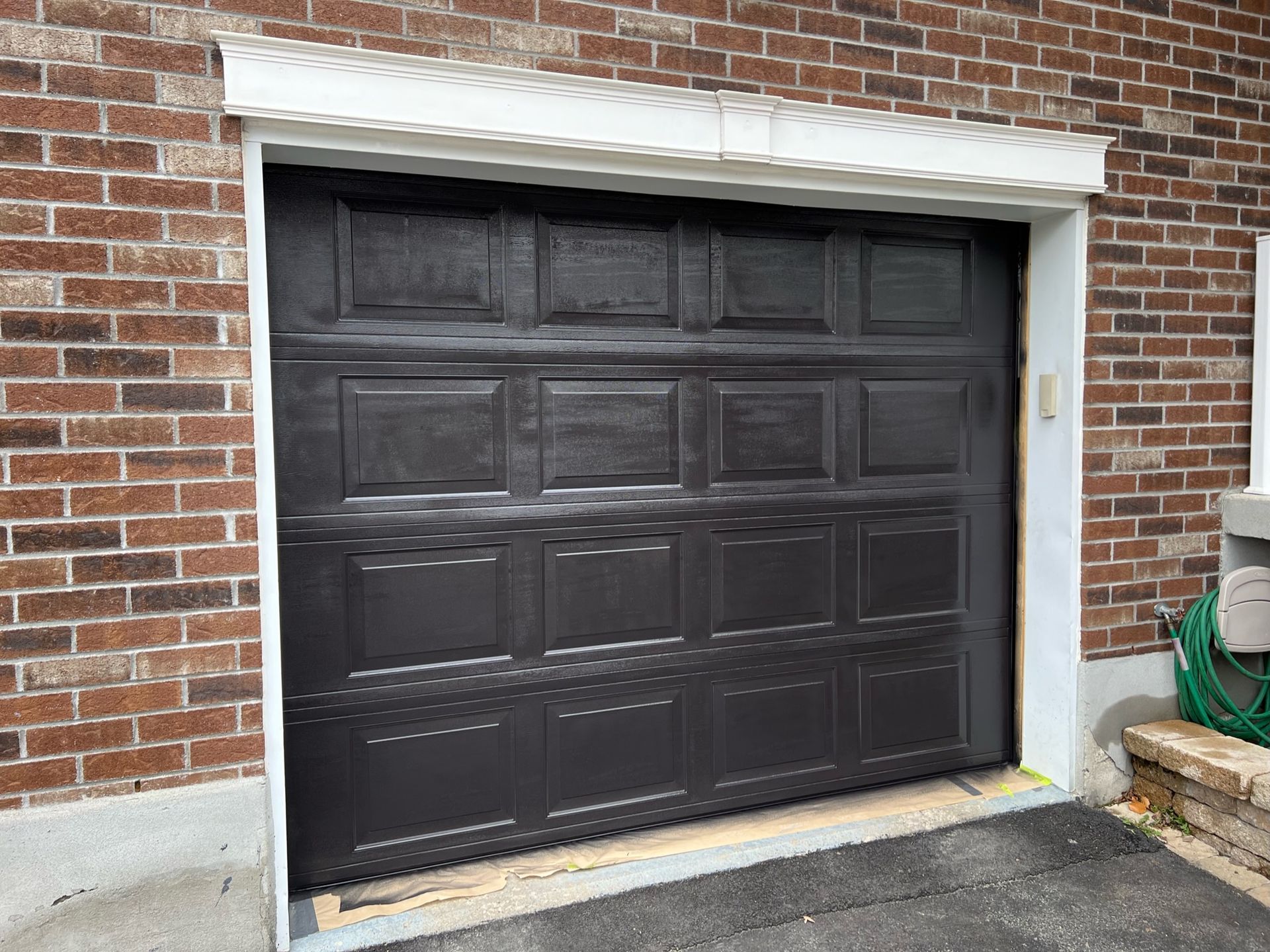 une porte de garage noire se trouve devant un bâtiment en brique.
