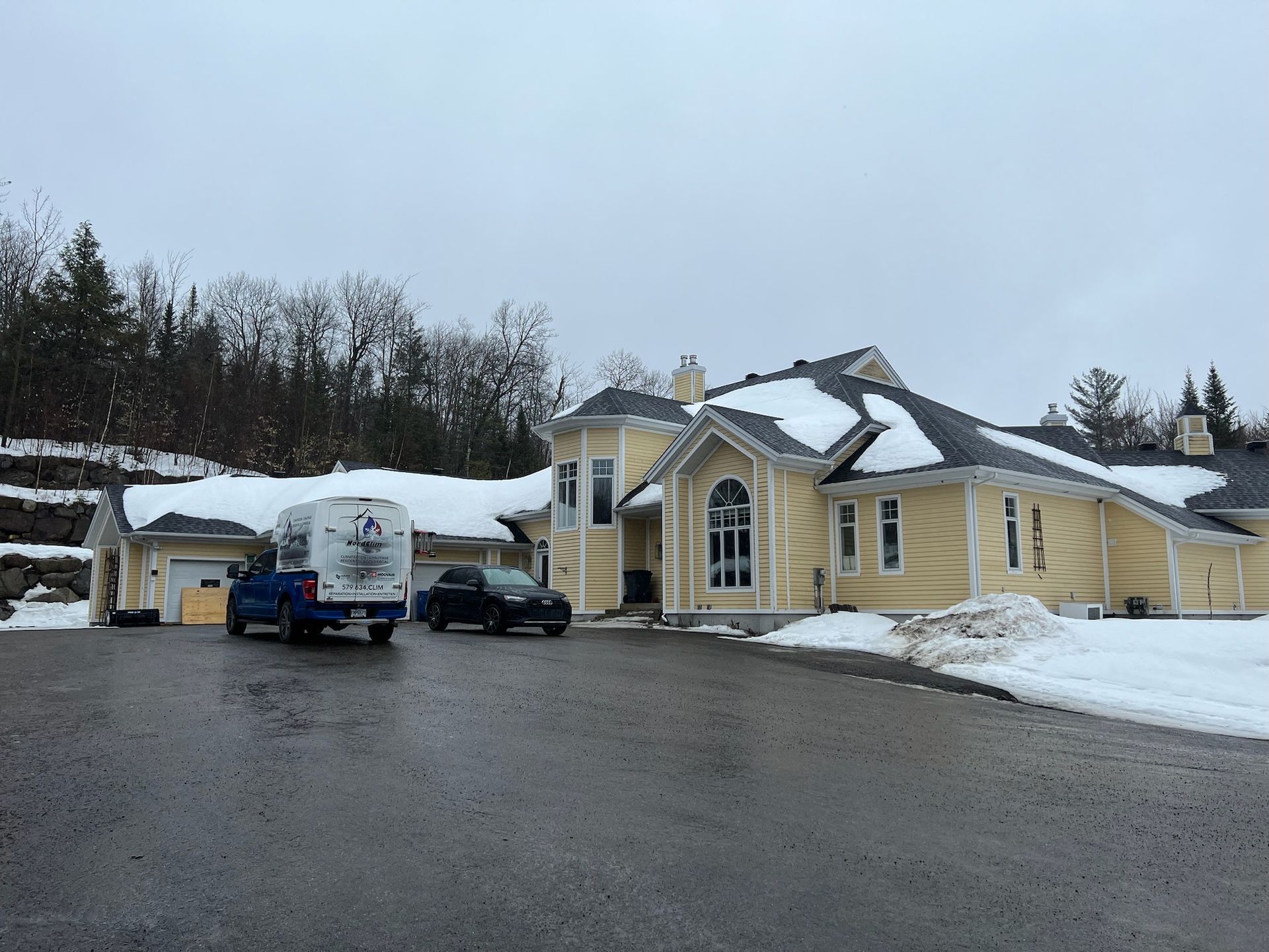 un camion bleu est garé devant une grande maison jaune recouverte de neige.