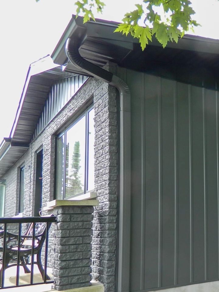 Bâtiment à façade noire avec finitions noires, piliers en brique, fenêtres et gouttière noire.