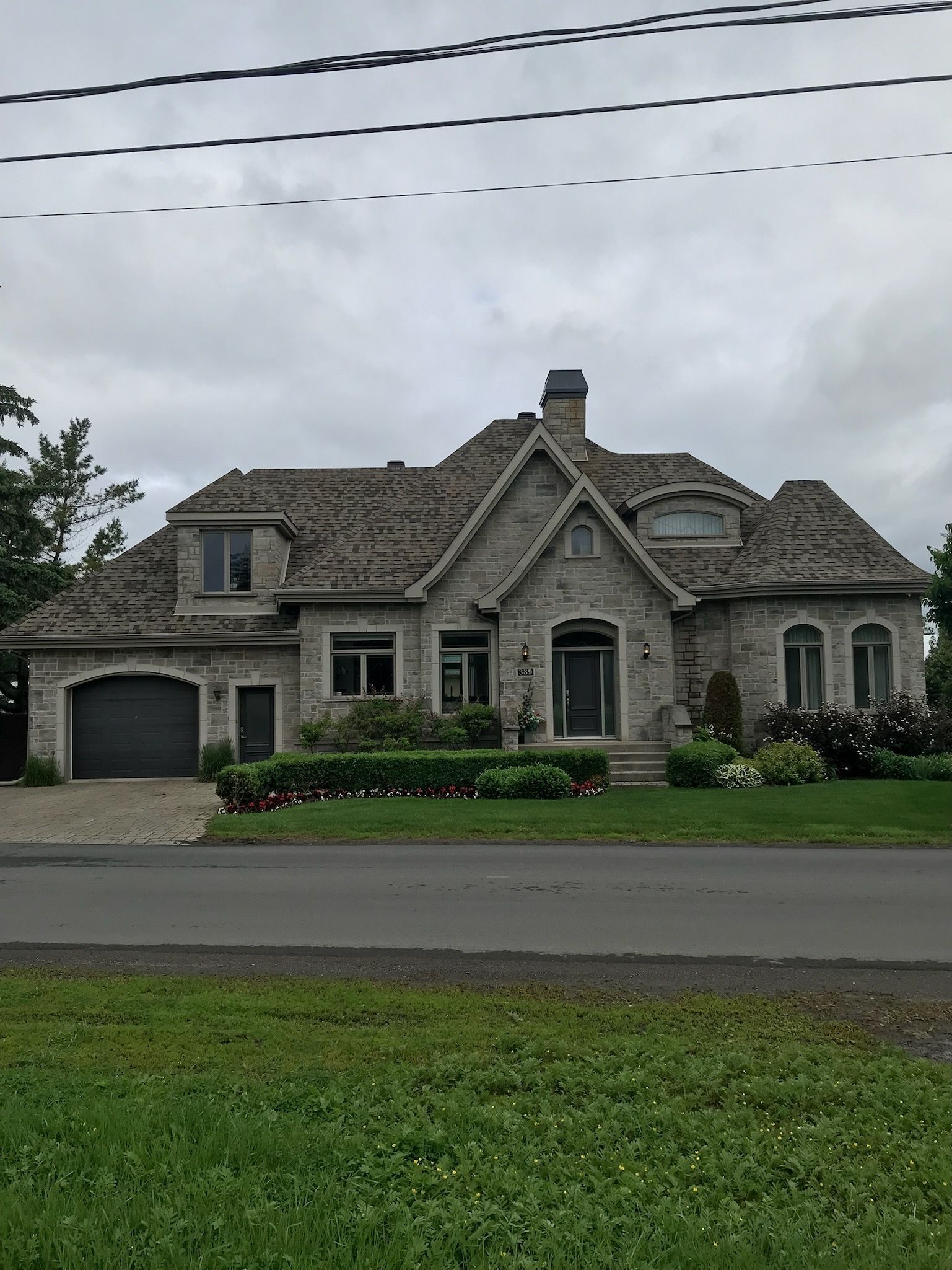 une grande maison avec un toit de bardeaux se trouve au bord de la route.