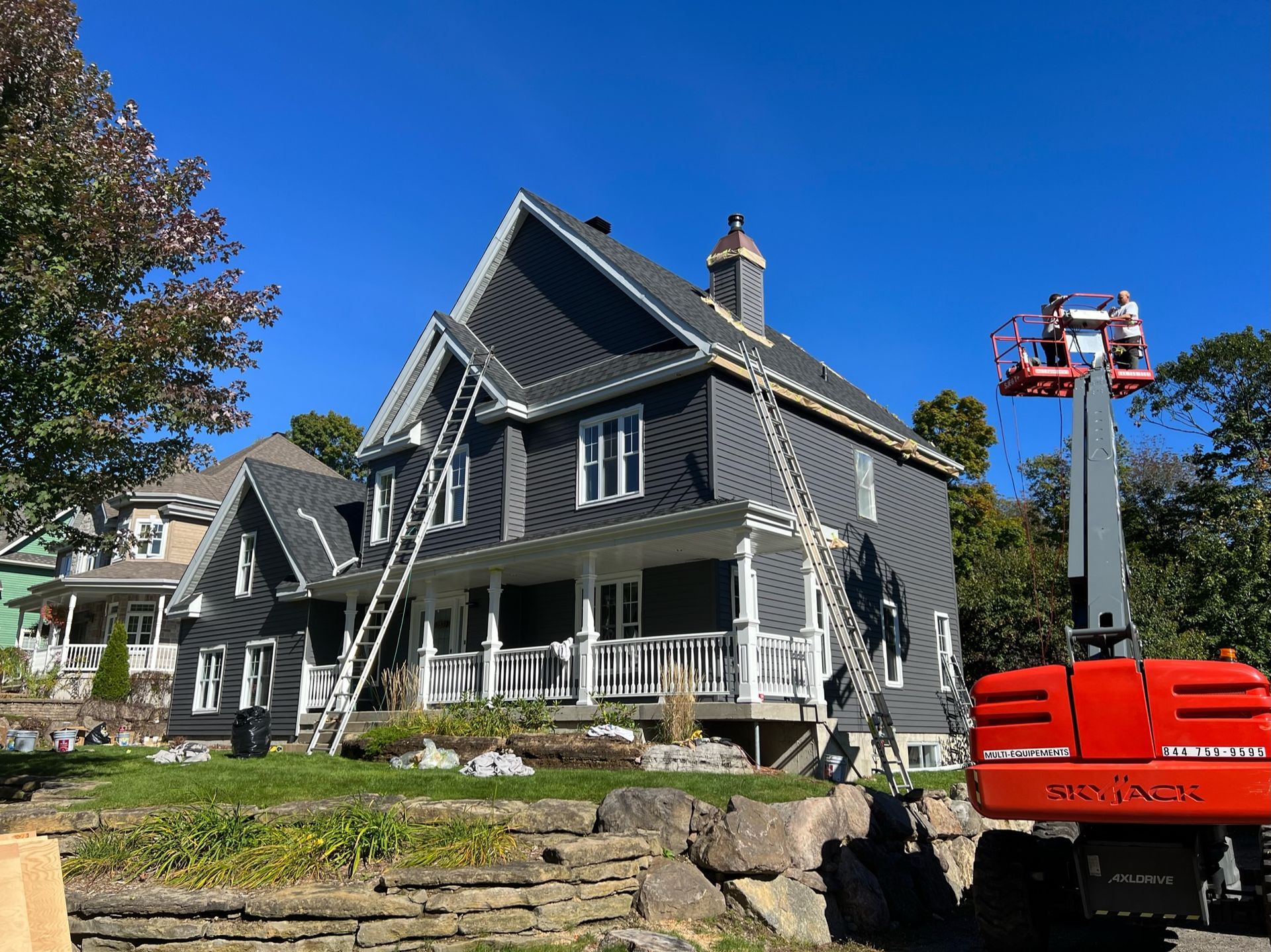 Extérieur d'une maison avec bardage gris, échelles et ascenseur. Ciel bleu en arrière-plan.