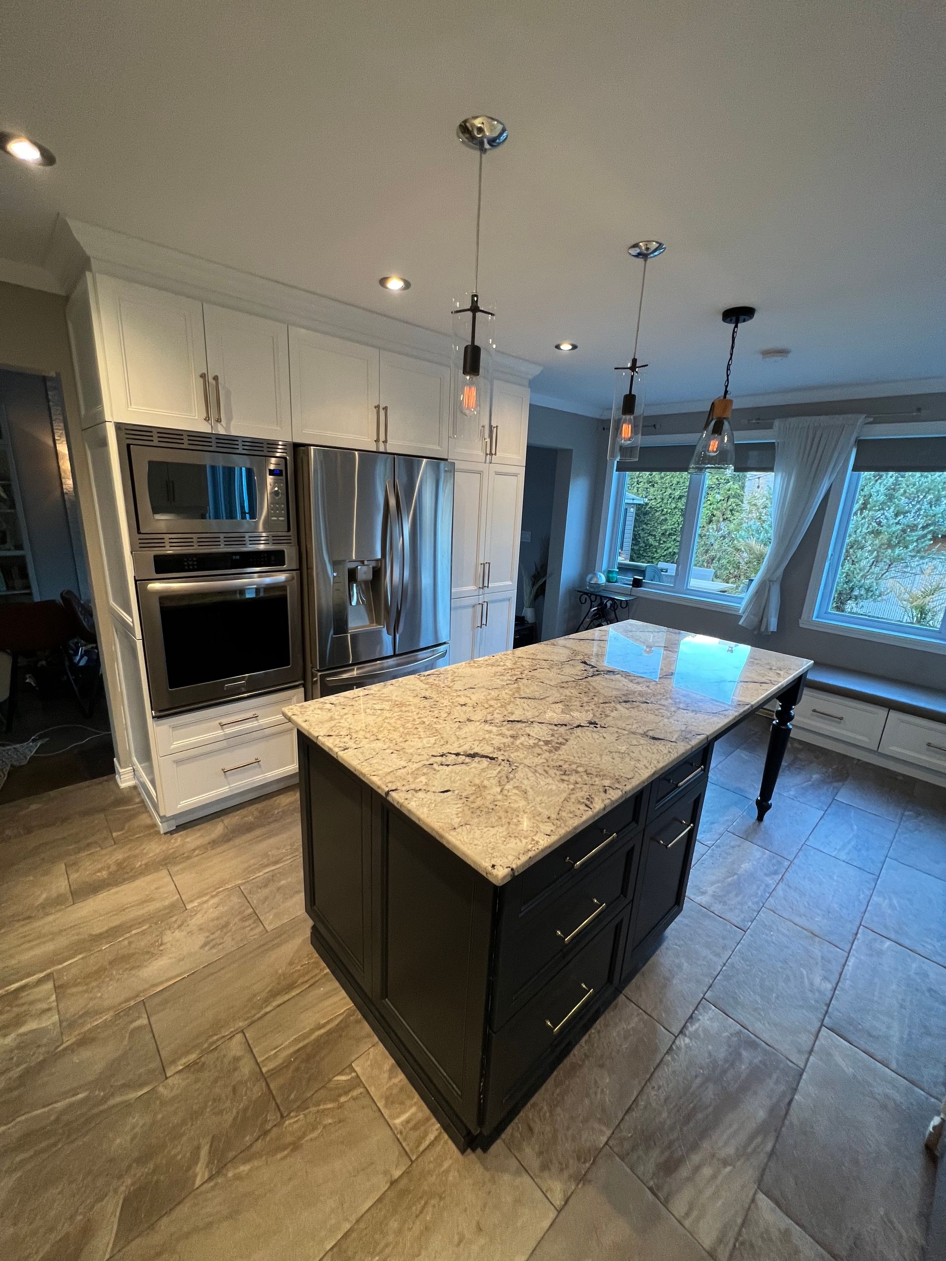 Une cuisine dotée d'un îlot central foncé avec un plan de travail en granit clair, d'appareils électroménagers en acier inoxydable et d'un sol carrelé.