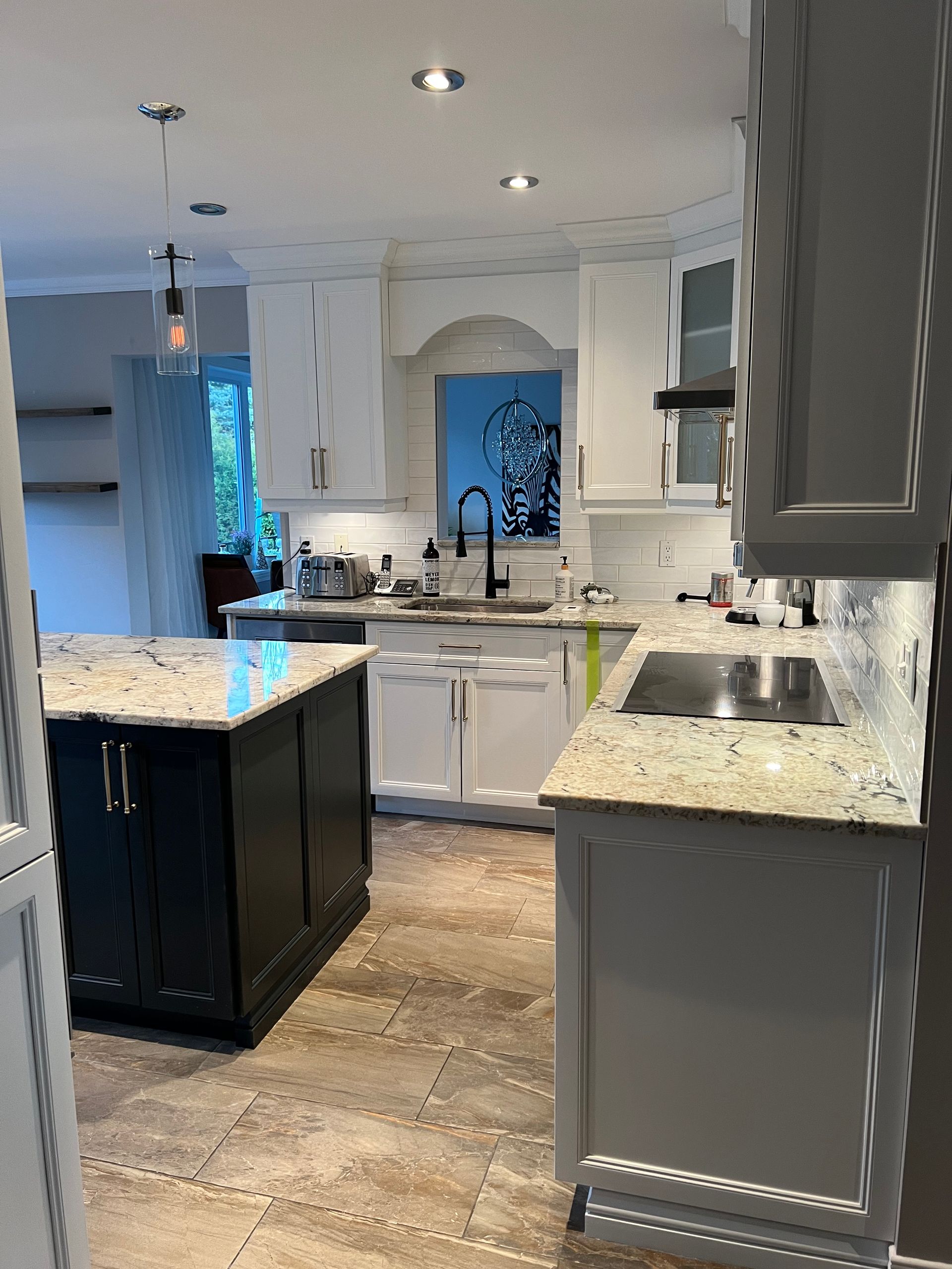 Une cuisine avec des armoires blanches, un îlot noir, des comptoirs en granit et un sol en pierre claire.