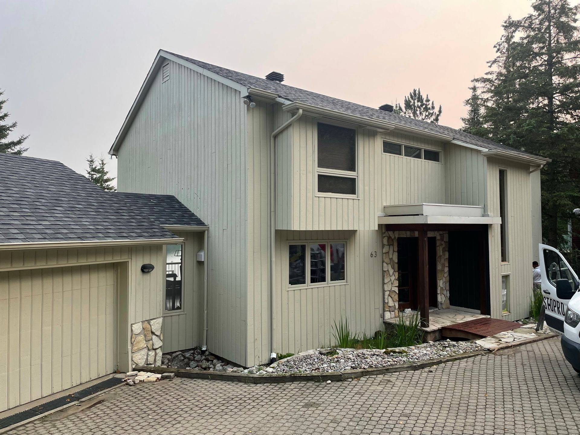 une maison blanche avec un toit noir et une camionnette blanche garée devant.