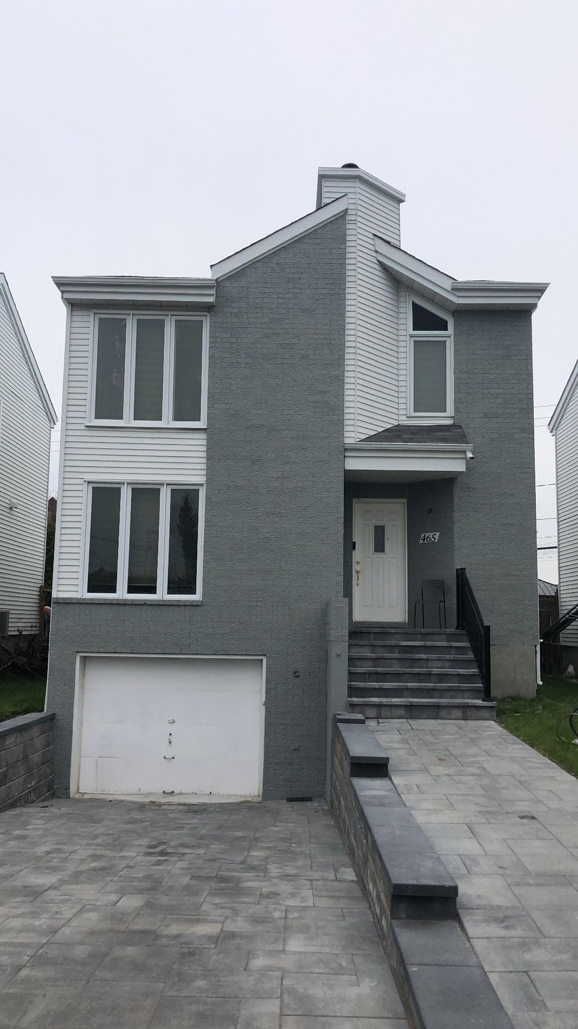 une grande maison en briques grises avec une porte de garage et des escaliers blancs.