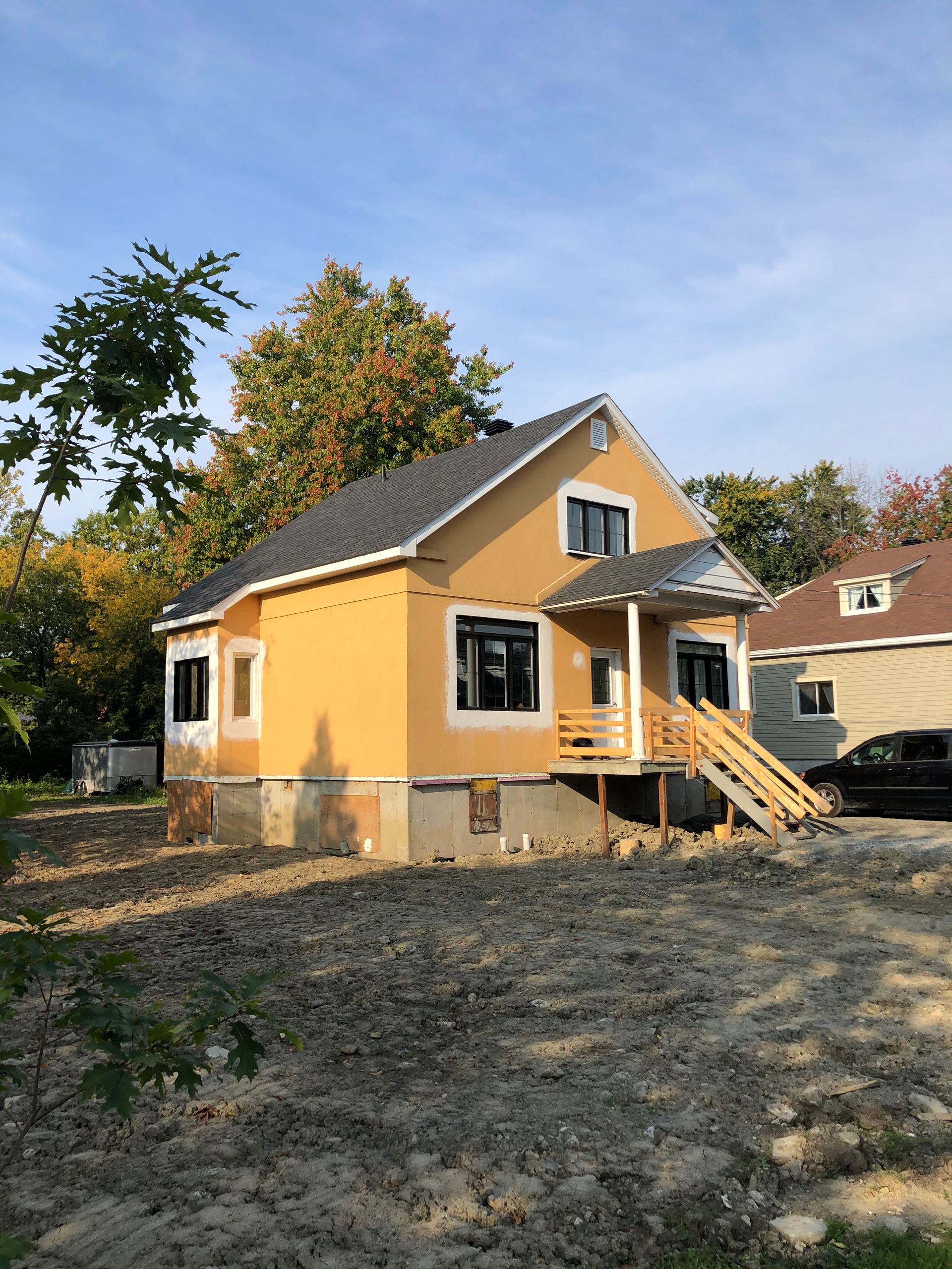une maison jaune avec un toit gris se trouve au milieu d'un champ de terre.