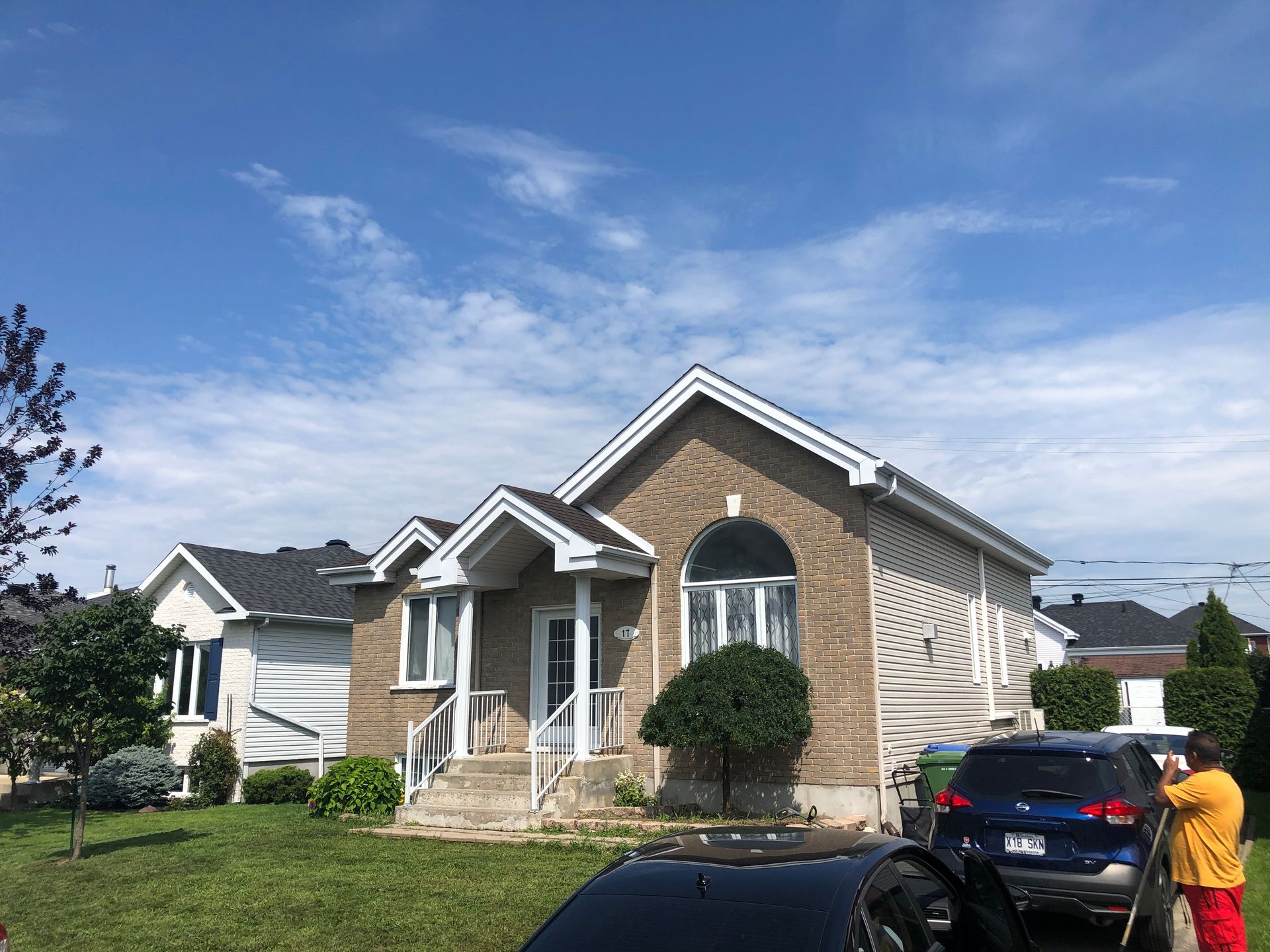 un homme se tient devant une maison avec une voiture garée devant.