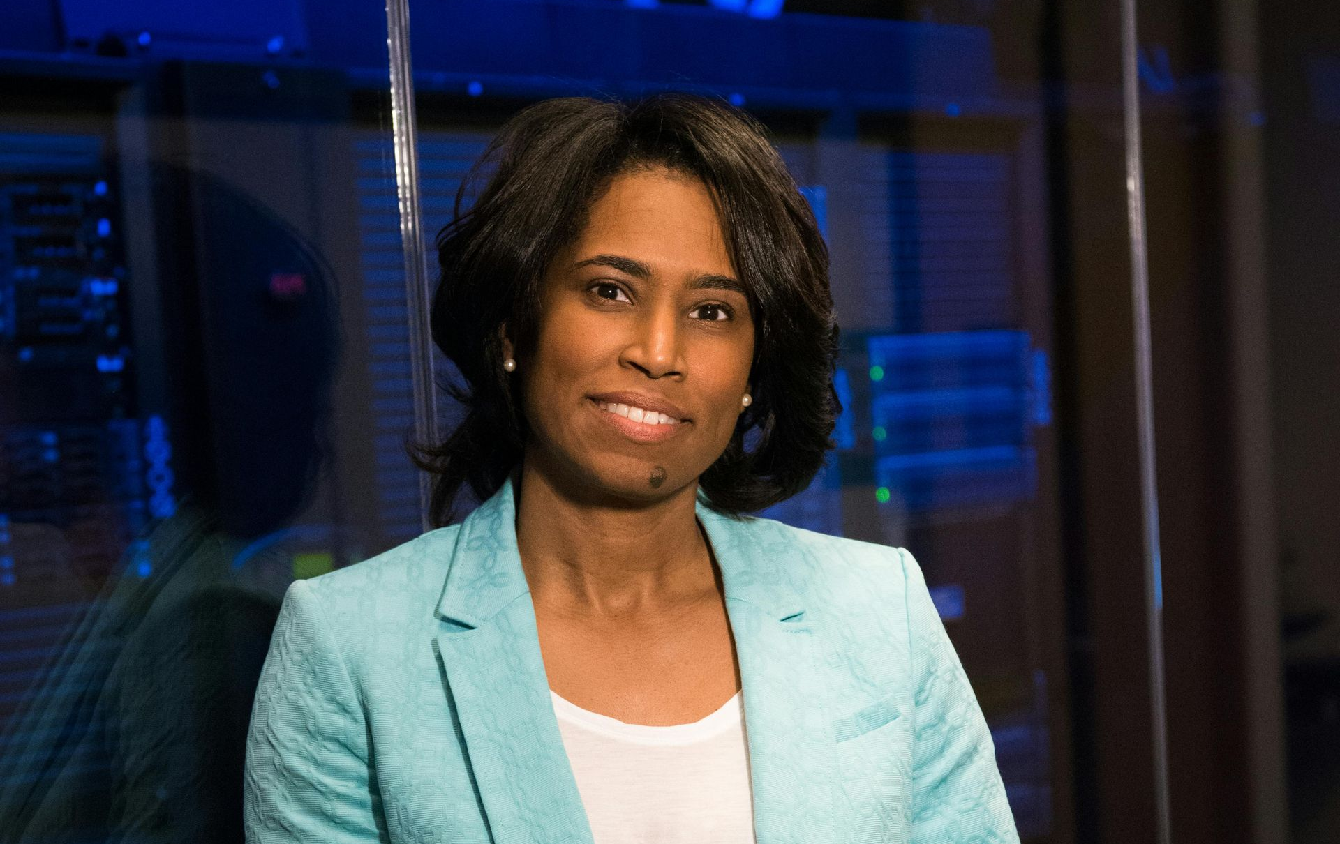 Woman in blue blazer, smiling, leaning against a data server.