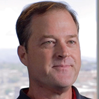 Woman with light brown hair, smiling, wearing a white collared shirt, outdoors on a foggy day.